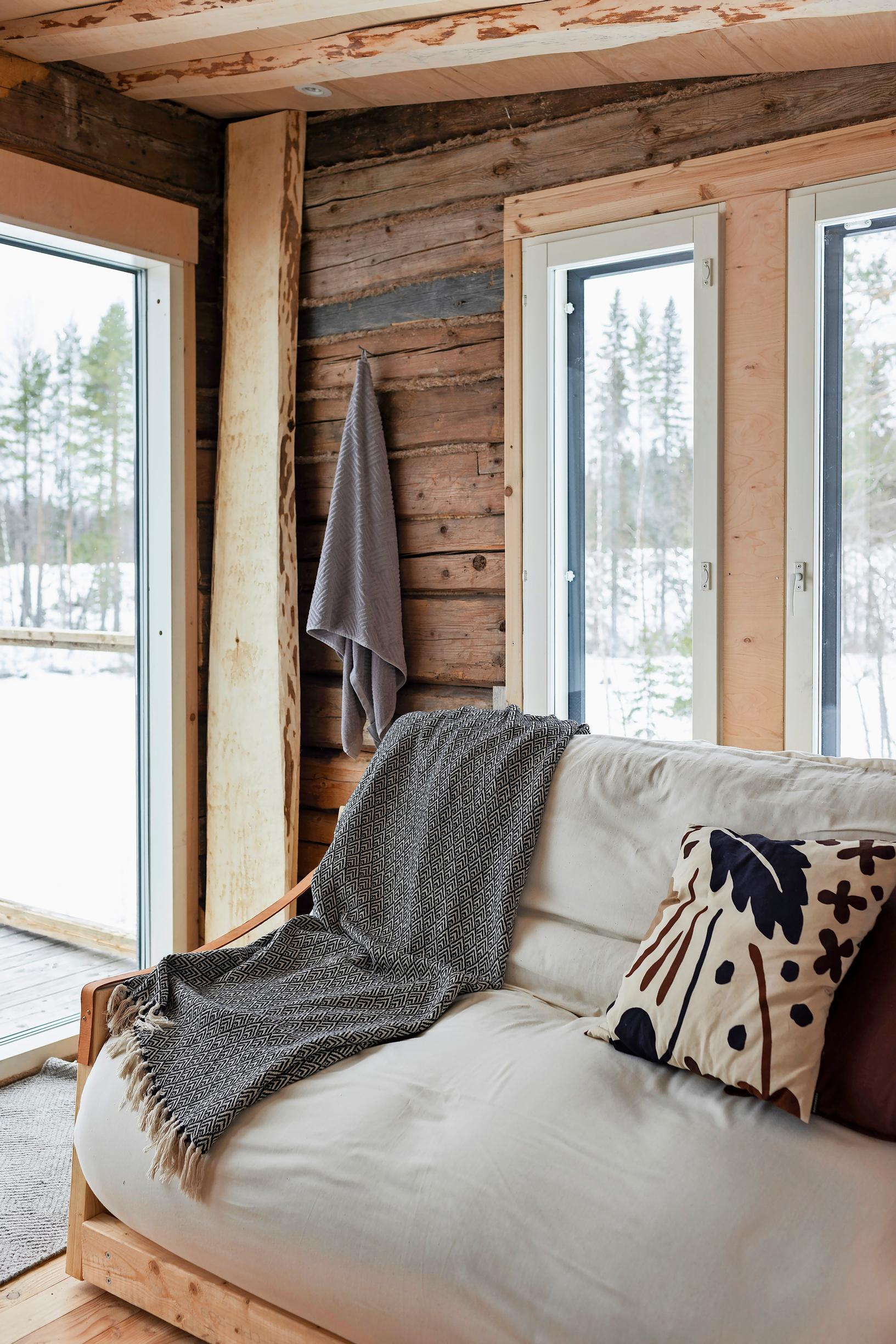 A light-colored sofa with a blanket and pillows, a hanging towel on the wall, and a snowy view through the windows.