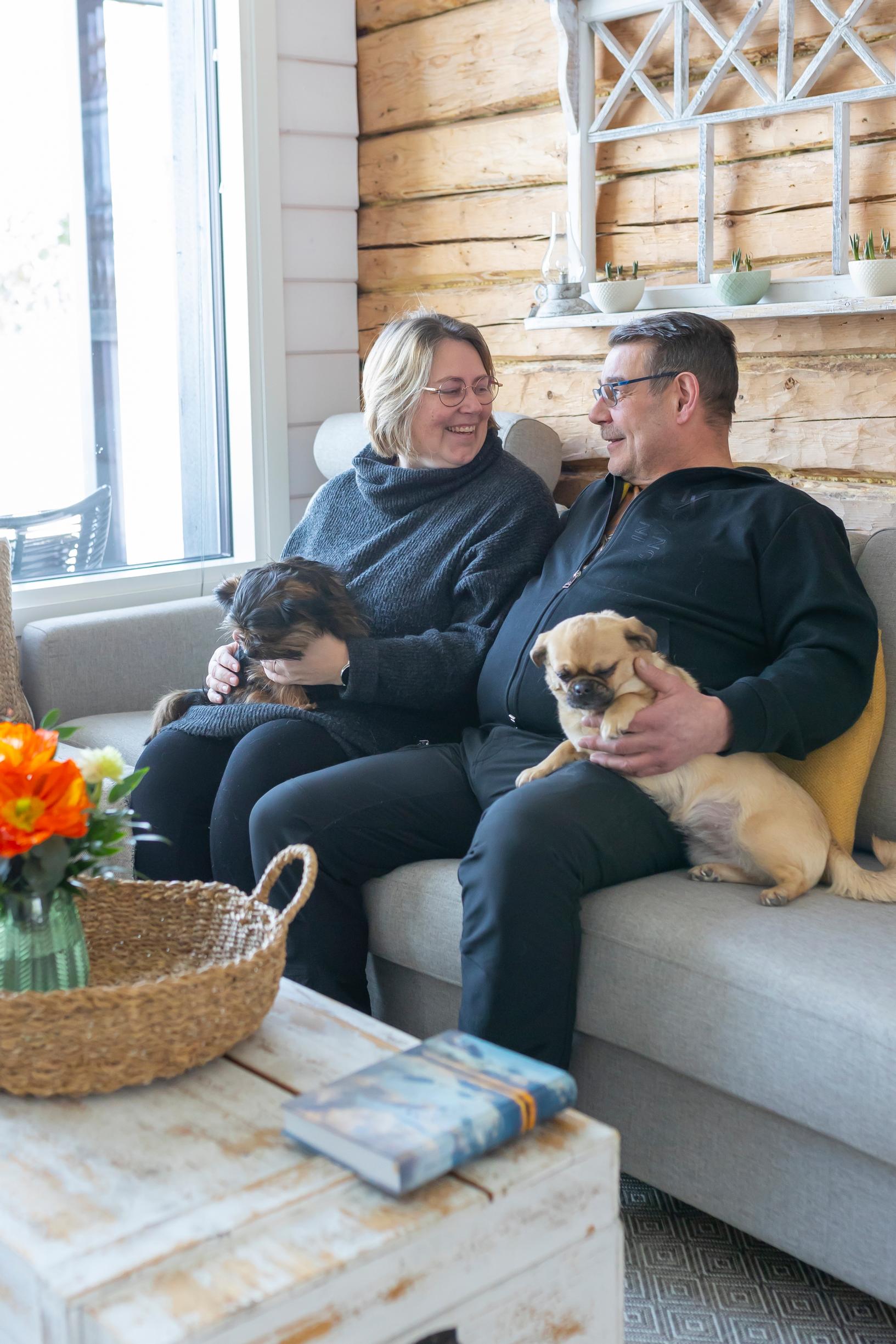 Mari and Kari on the sofa, each with a small dog beside them; a chest in front and a log wall in the background