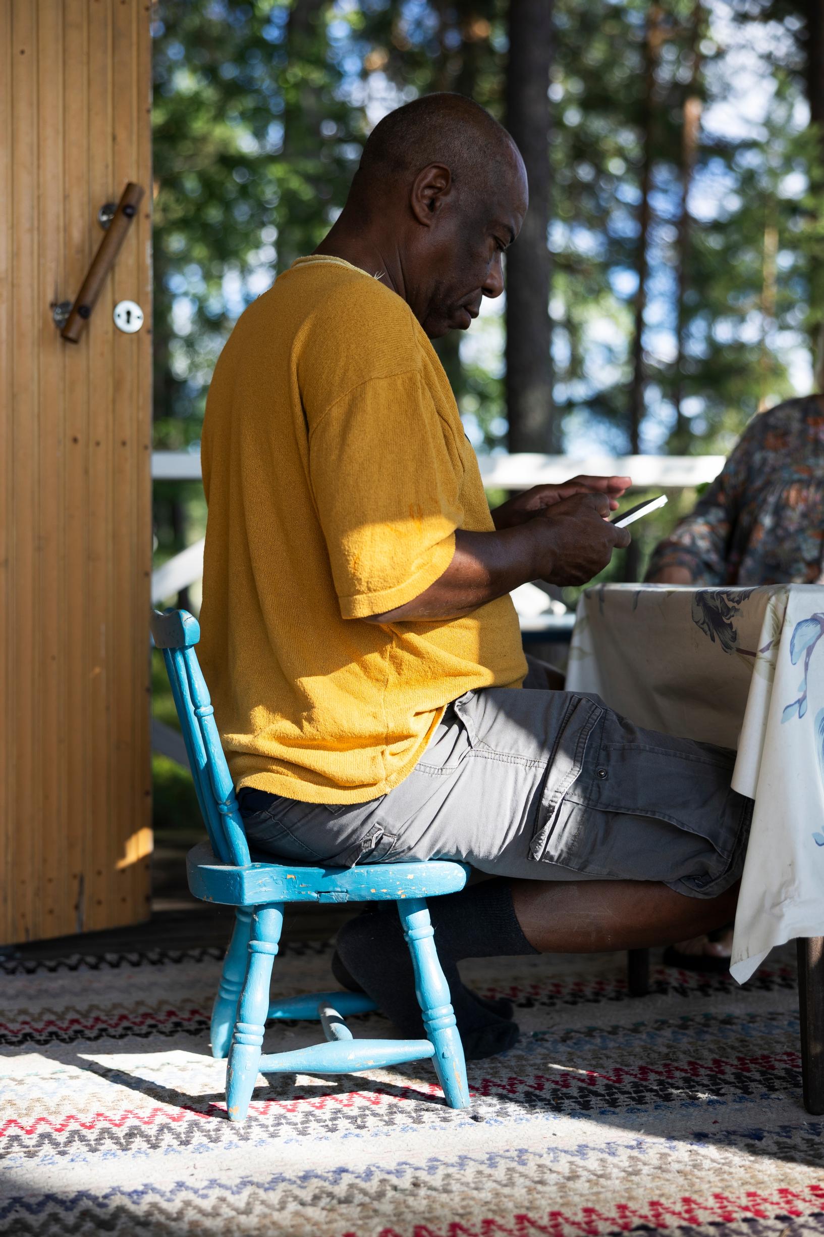 Edson sits on a turquoise small chair on the terrace