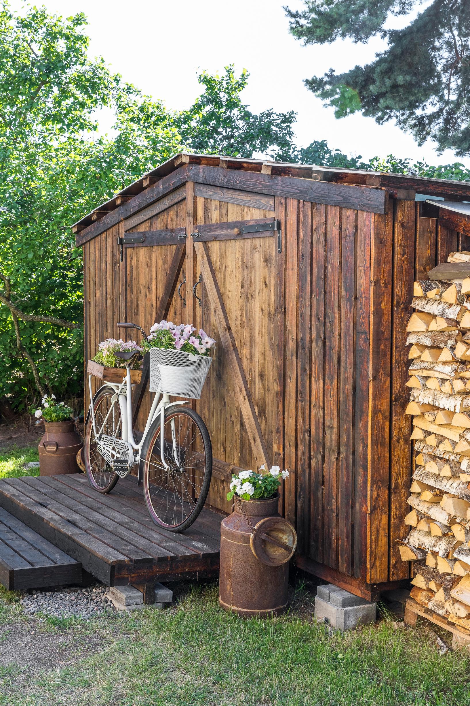 A garden shed with summer flowers in an old bicycle and milk cans in front