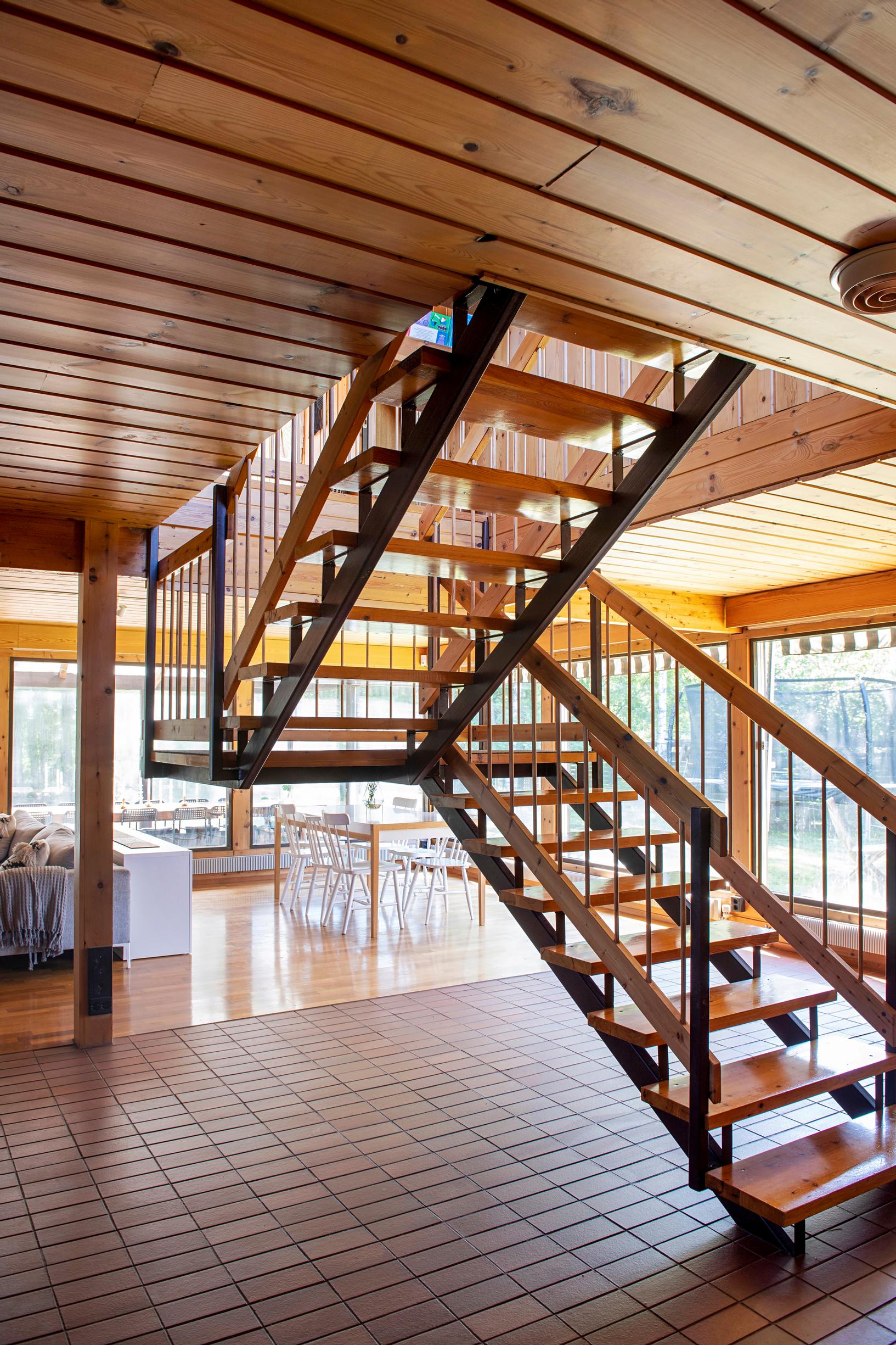 The walls of this spacious room are made of large windows. In the center is an airy metal-framed staircase.