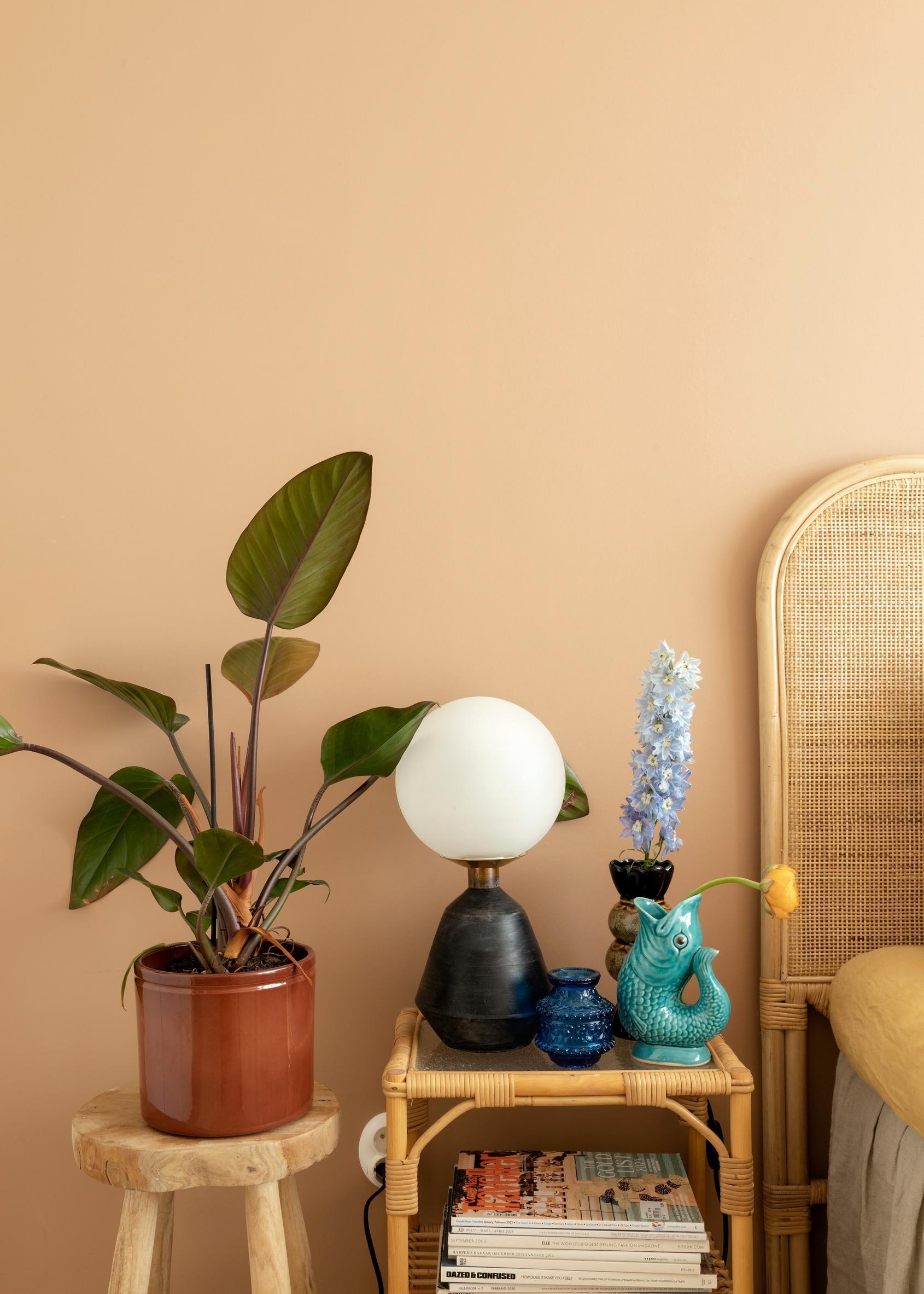 Rattan bedside table and a stool with a houseplant next to the bed.