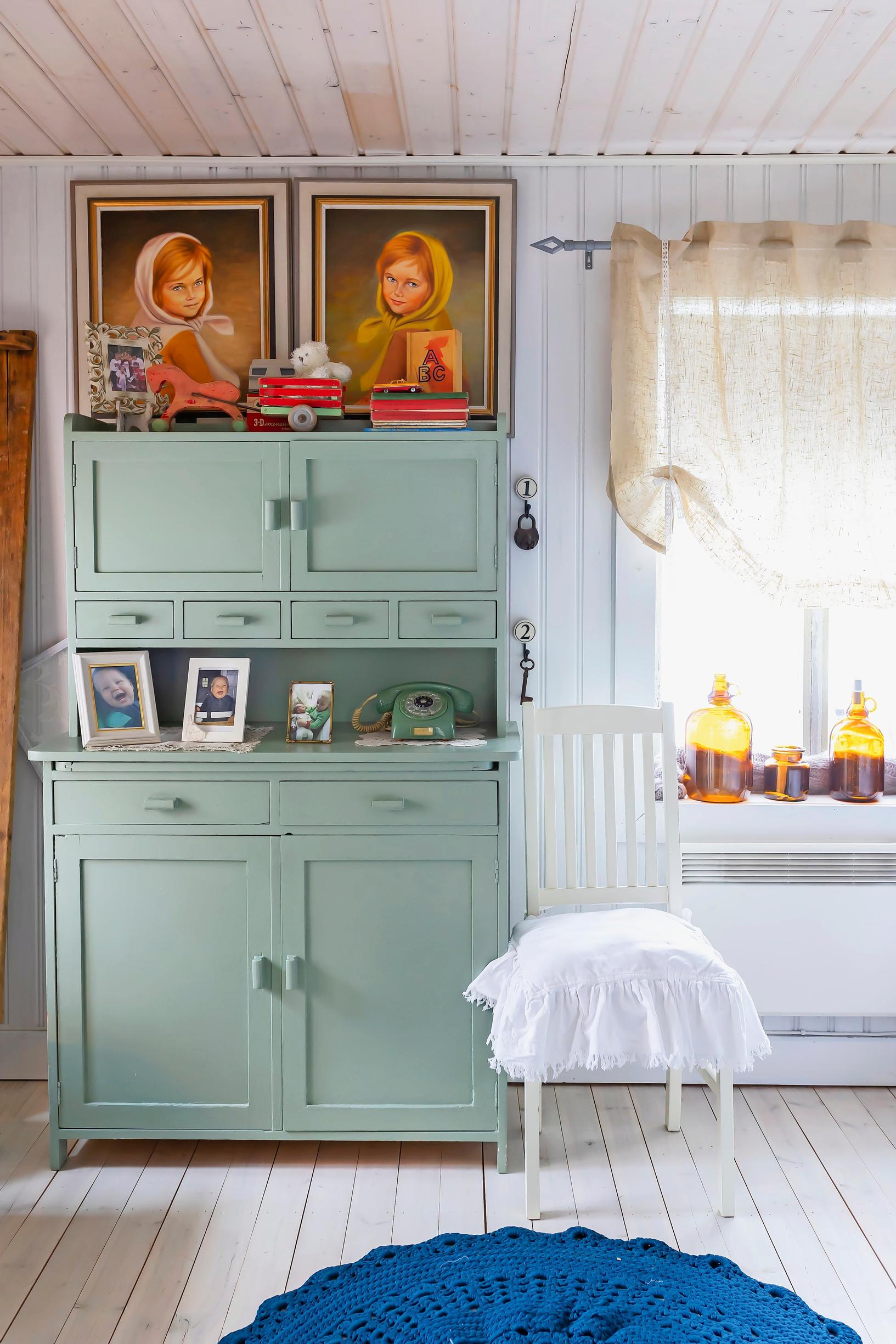 an old green china cabinet, paintings, and a plank floor