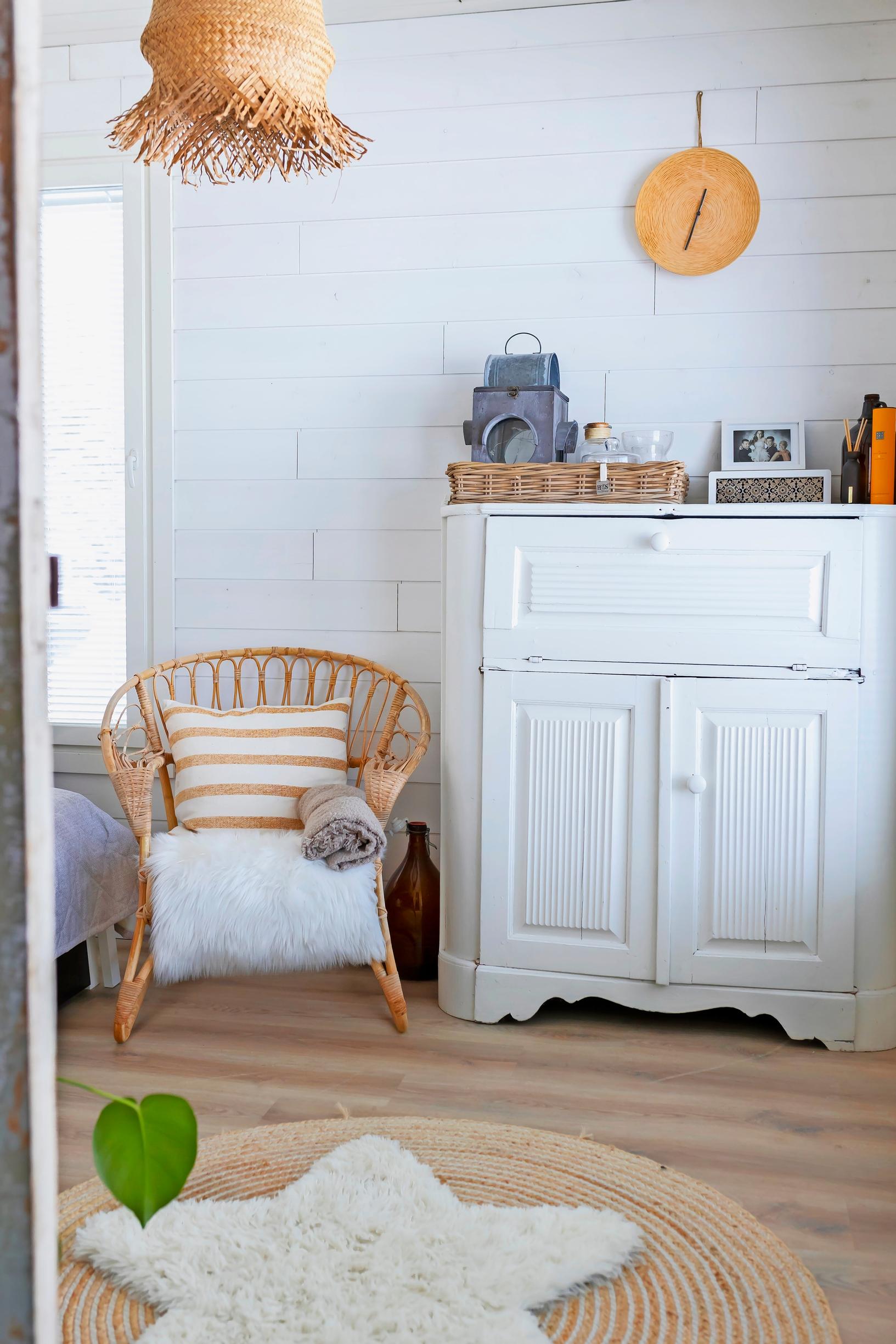 Rattan chair, cushion, rug, white dresser, and white wooden wall