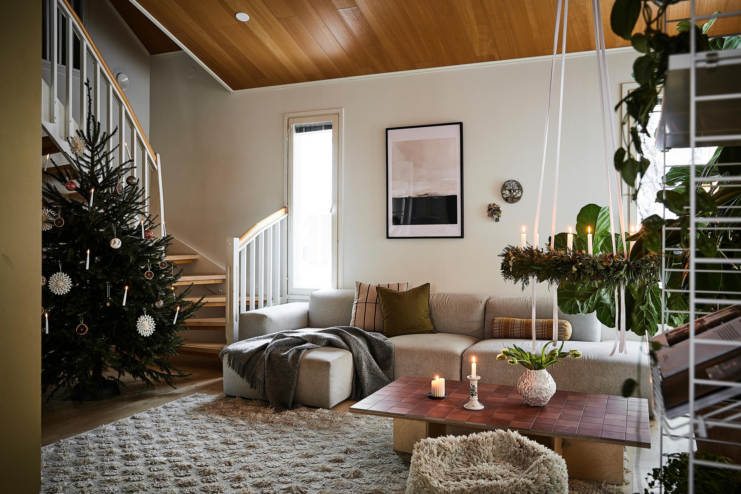 A Christmas tree, staircase, light-toned corner sofa, coffee table, and shelving unit