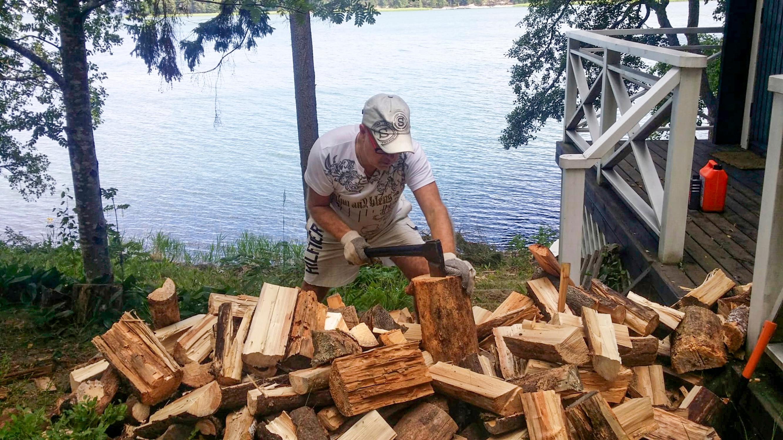 Singer Petri Laaksonen stands by a wood pile at the seashore, holding an axe. Next to him is the sauna terrace