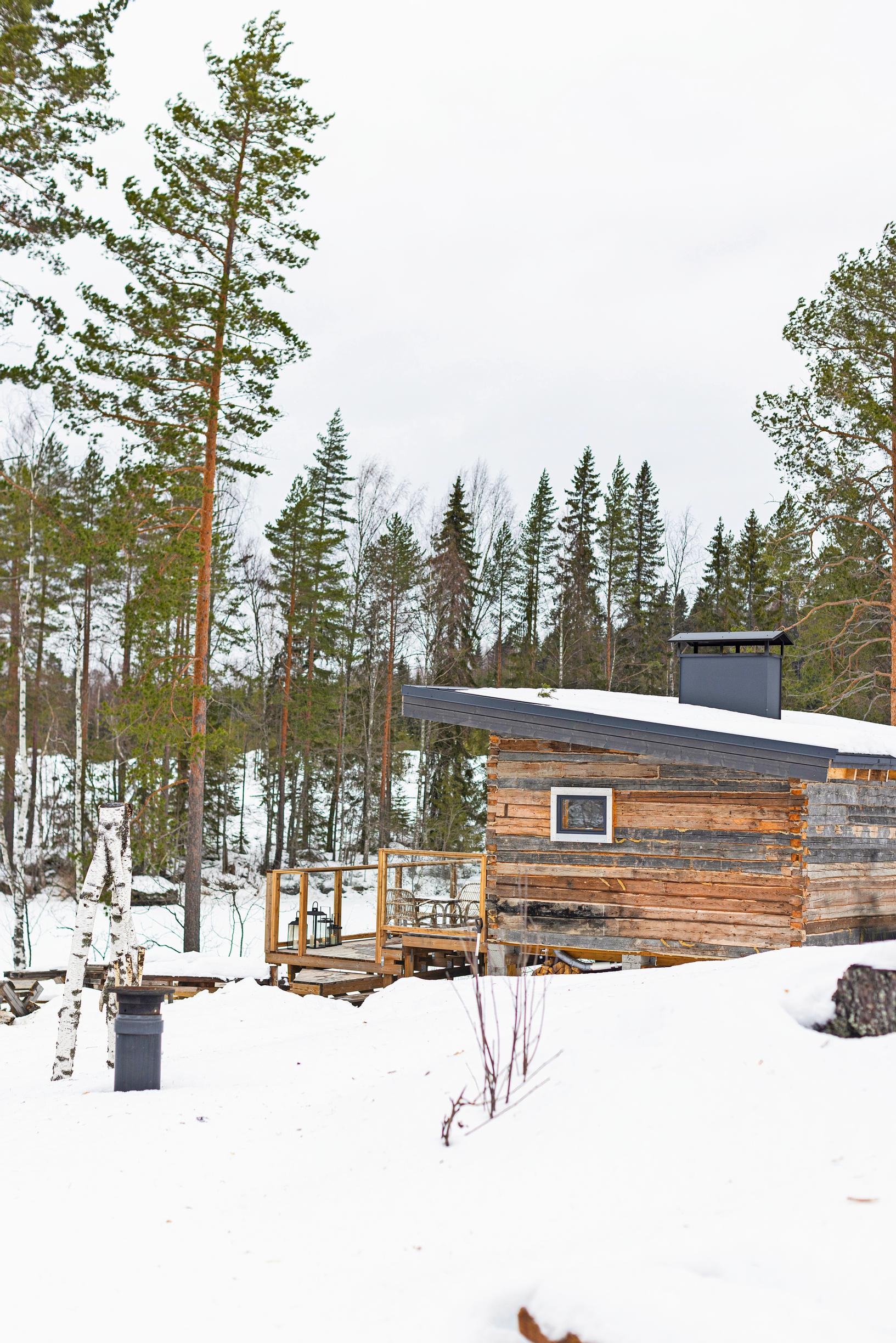 An old log building by a snowy lakeside, with a forest opposite the shore.