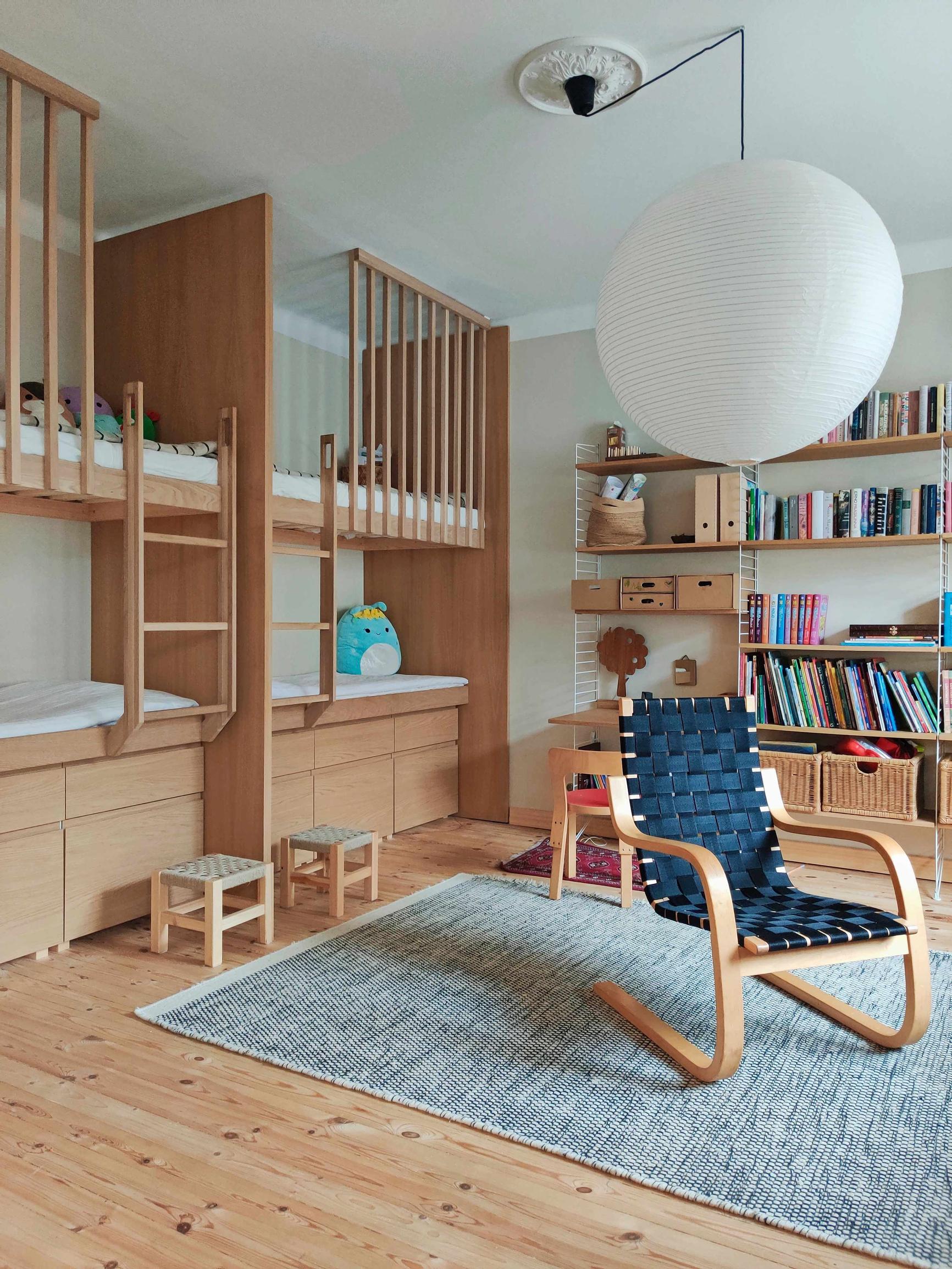 a four-person bunk bed, a large rug, and an Artek chair. a bookshelf is visible in the background