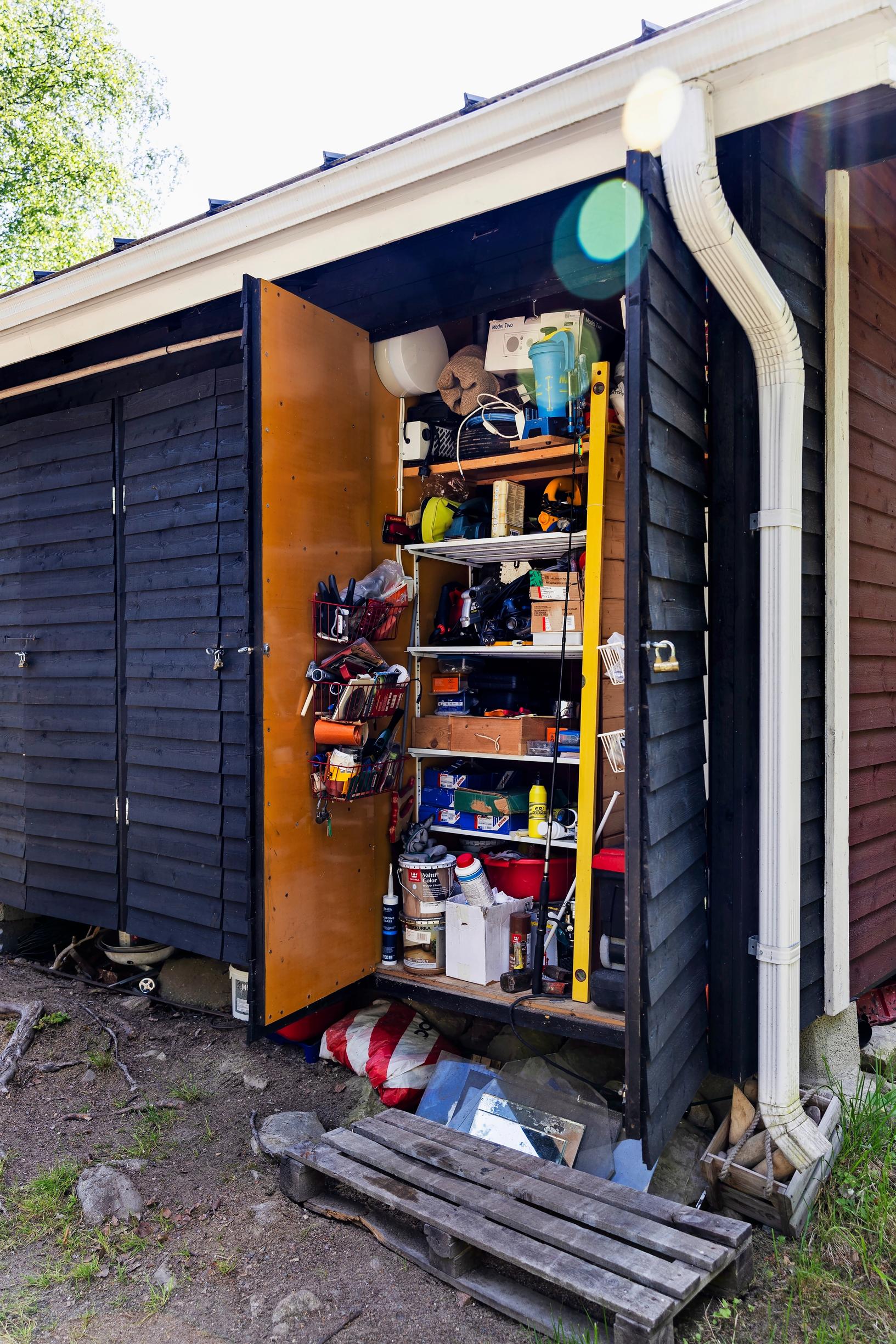 a storage cabinet attached to the dark log cottage wall, filled with items, doors open