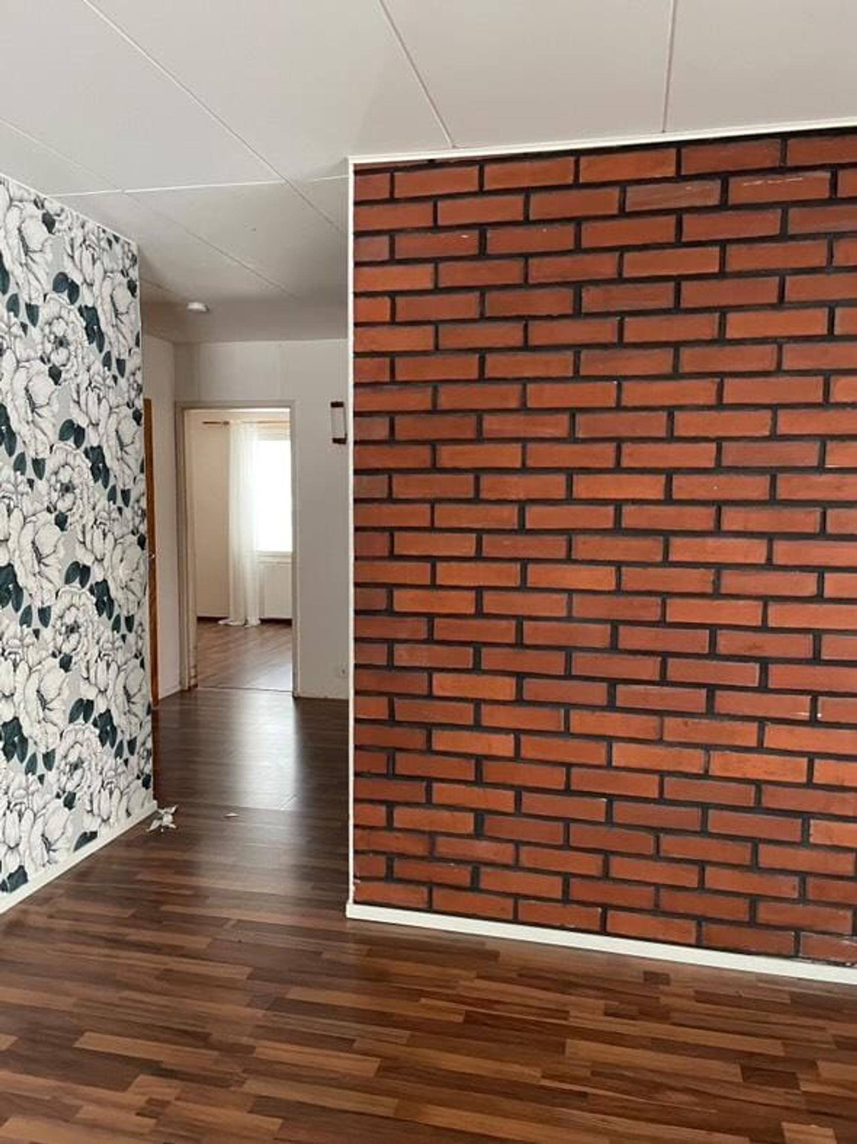 In this room, there’s a dark parquet floor, a brick wall, and an accent wall covered with patterned wallpaper