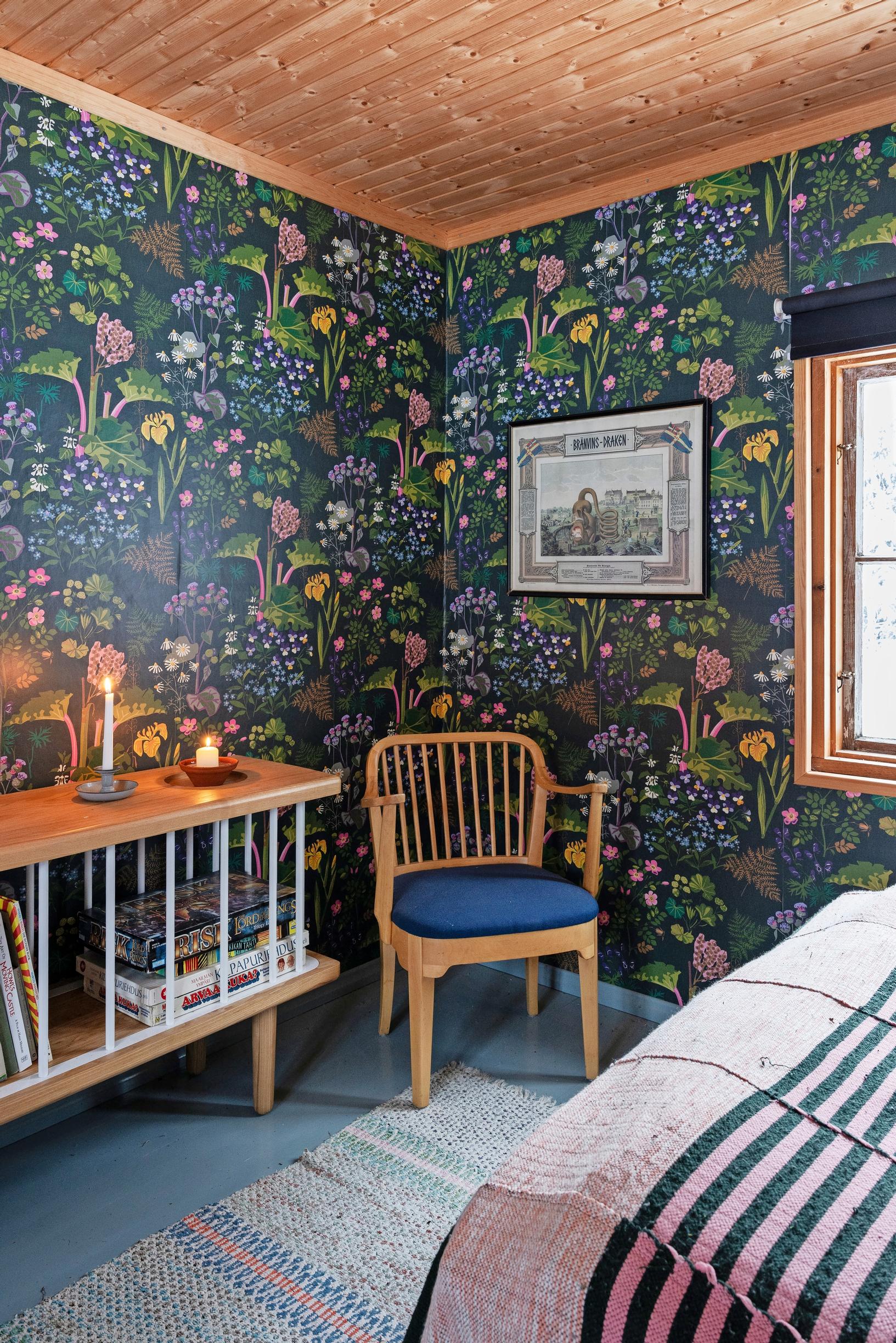 Dark patterned wallpaper, rag rug, wooden chair, candles on a shelf, and a bed
