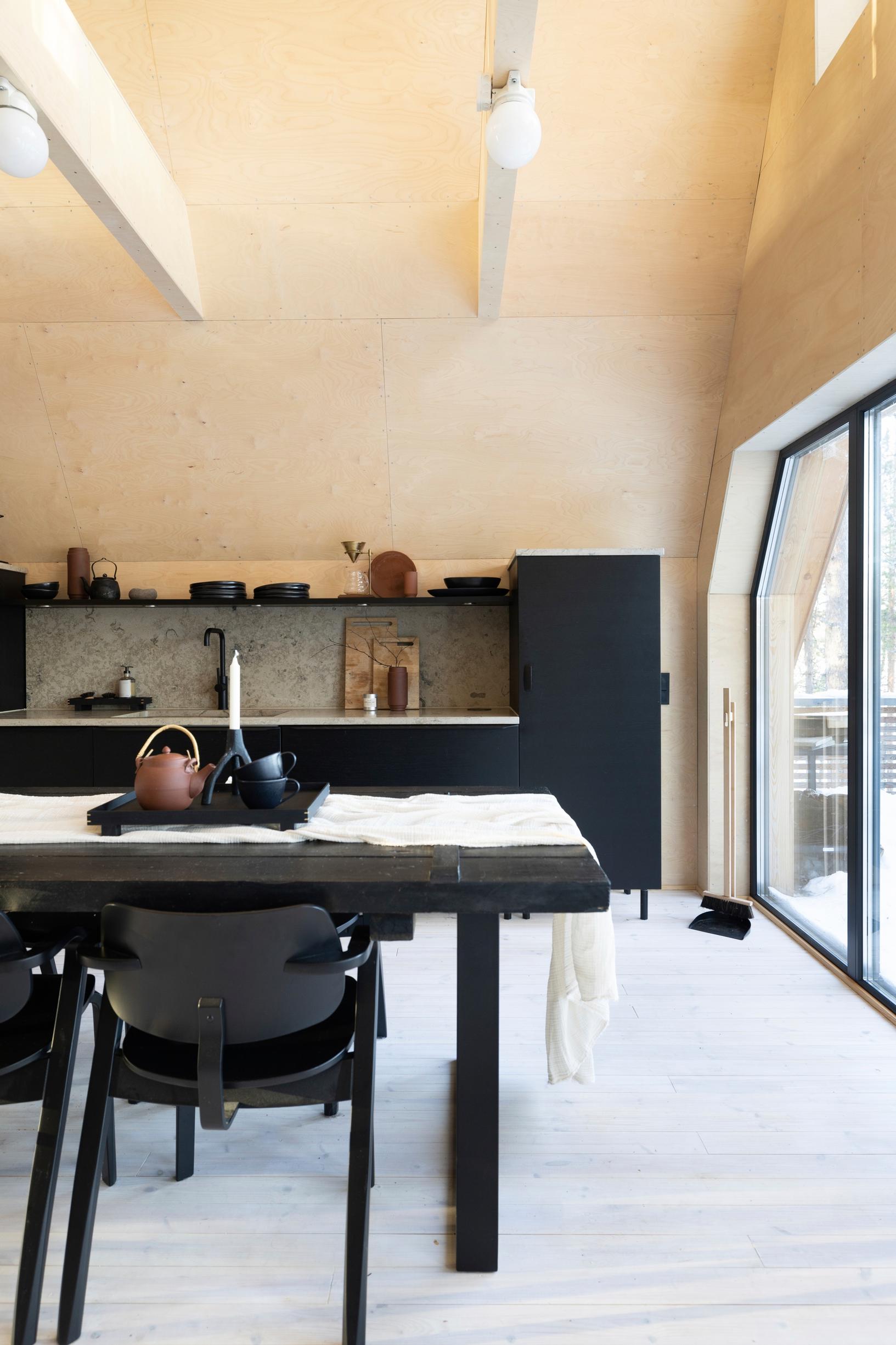 Black kitchen in a light, wooden-walled space