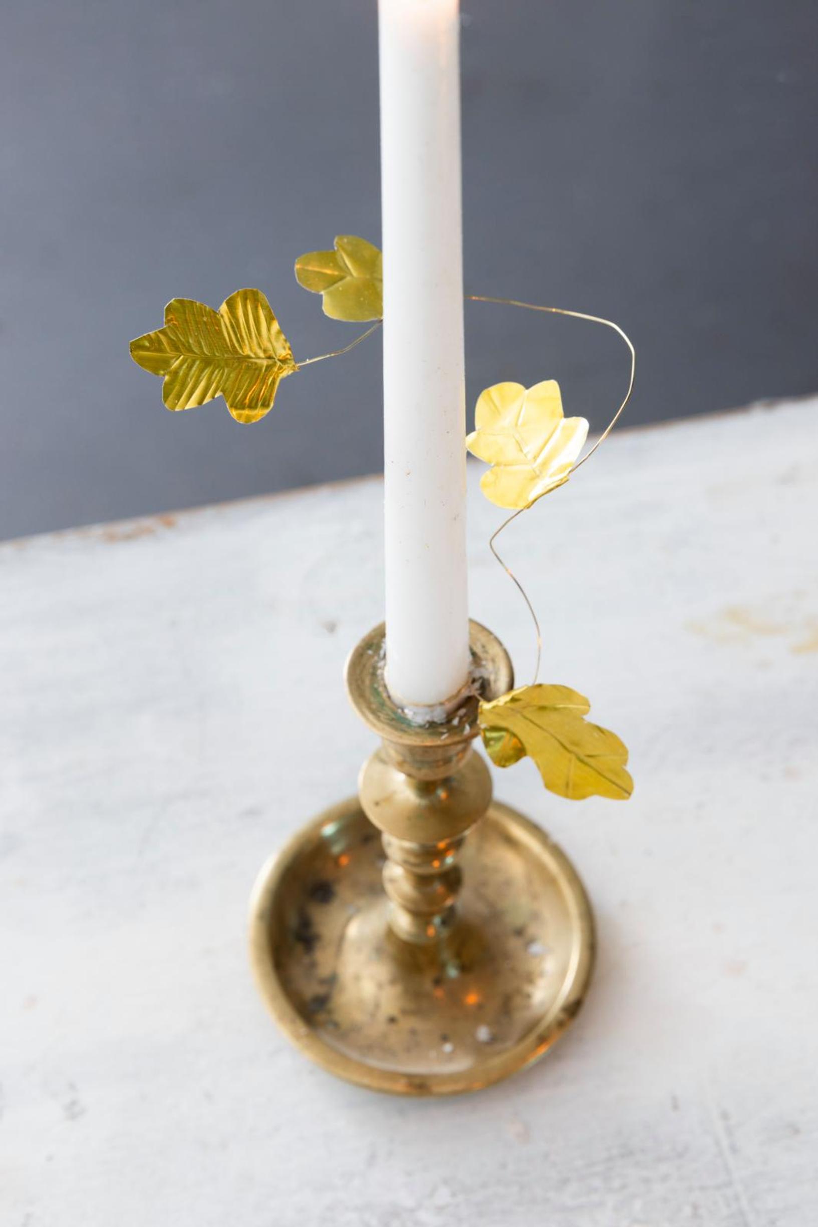 The candle is adorned with a metallic leaf garland.