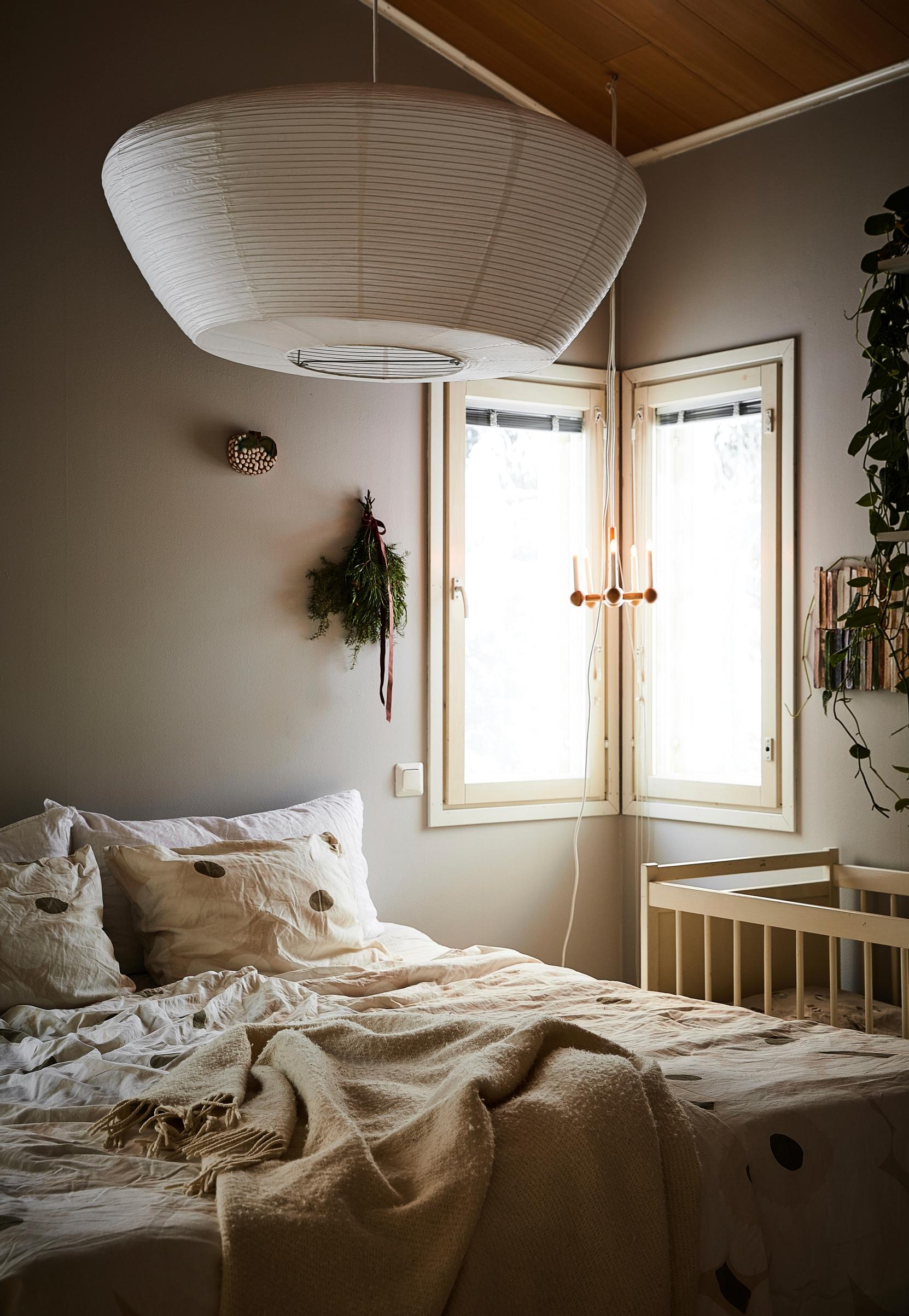 A light-colored bedroom with a large ceiling lamp, corner window, and crib