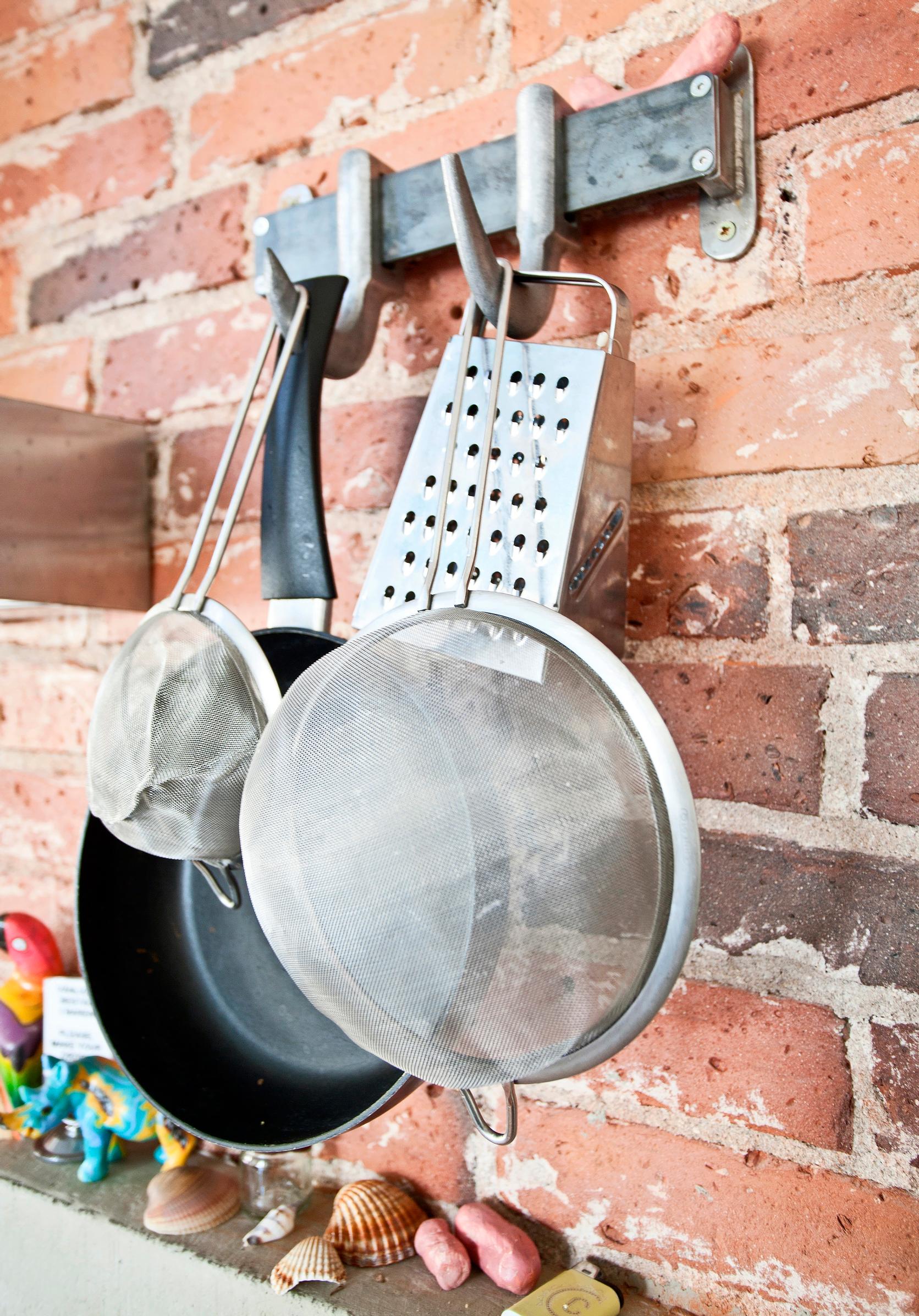 A frying pan and strainers hanging from meat hooks