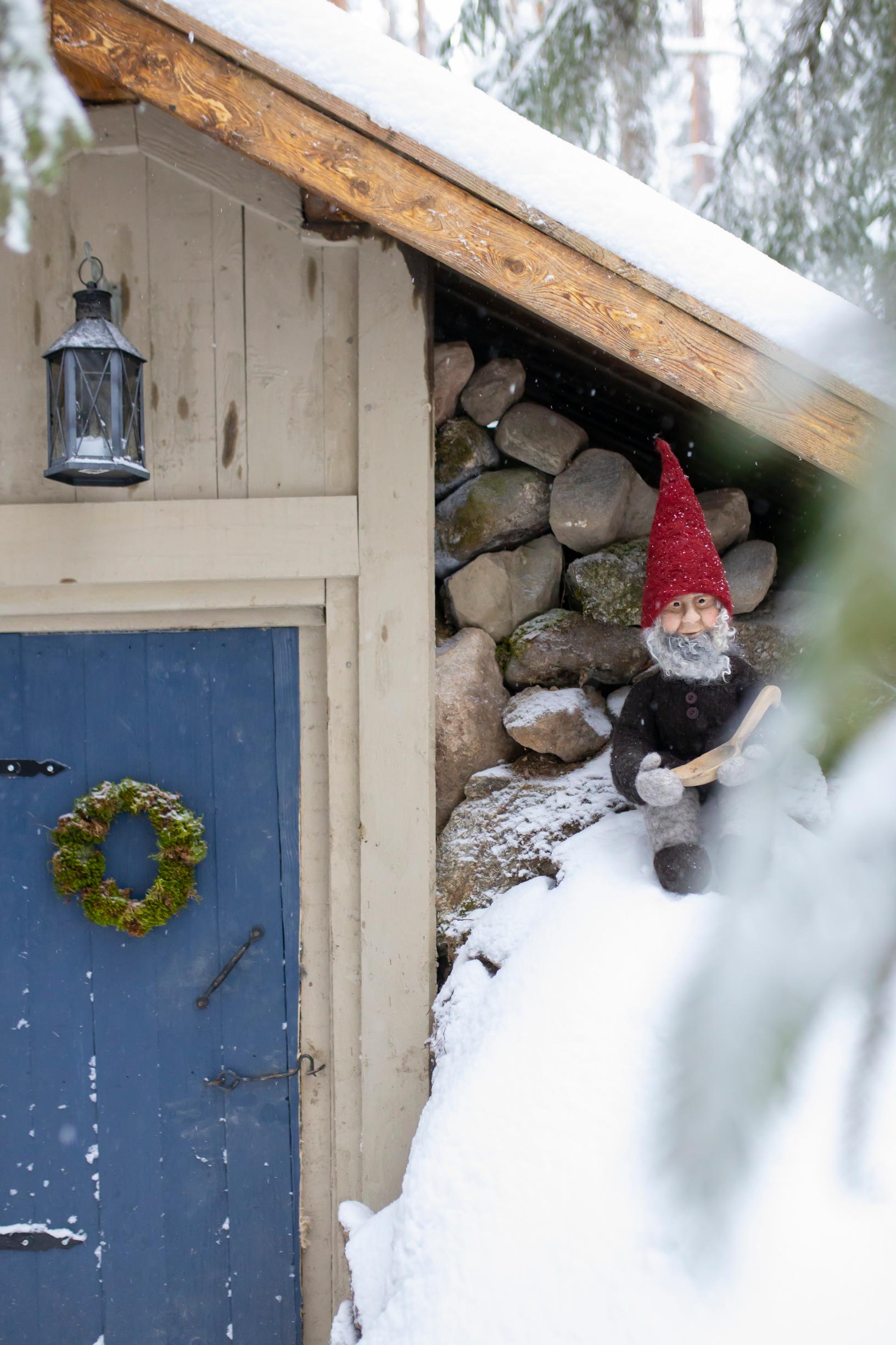 A gnome ornament in the snow by the root cellar door.