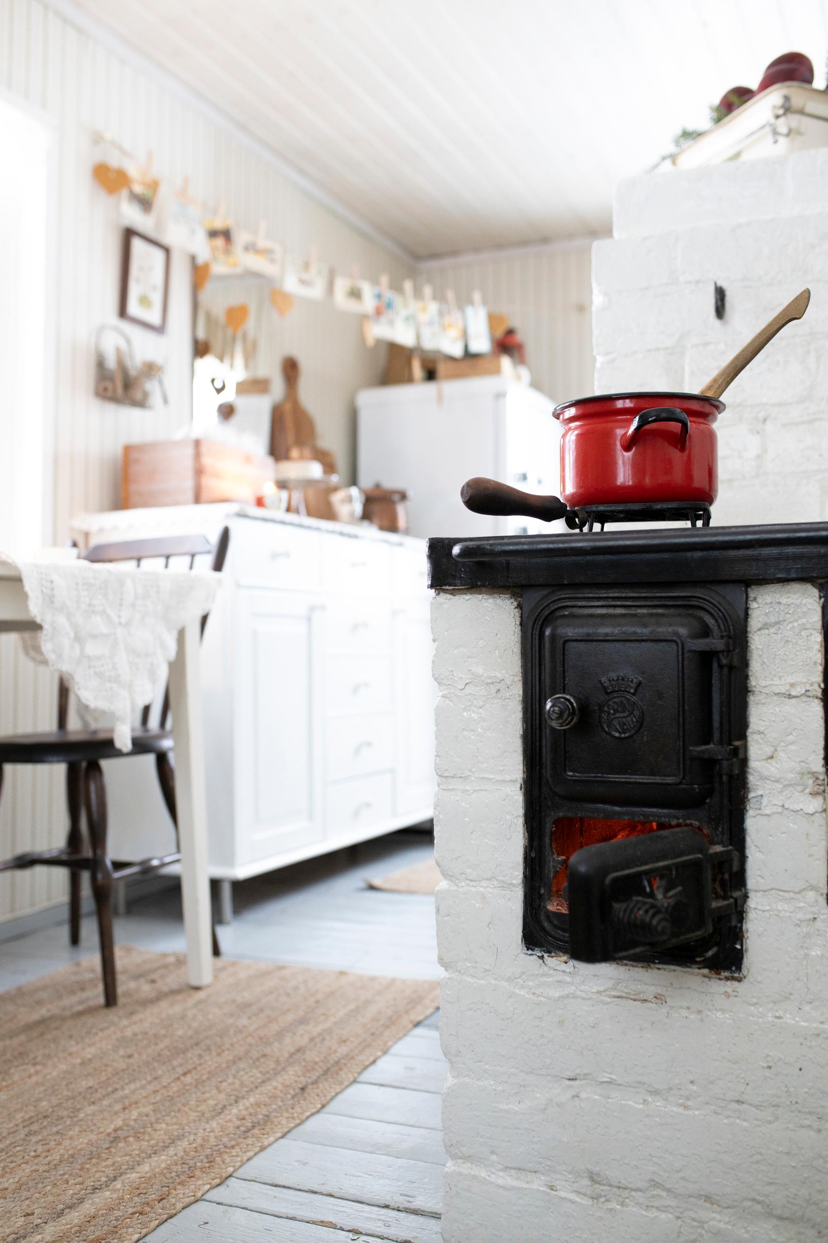 A white wood stove in the kitchen, with a red pot on top.