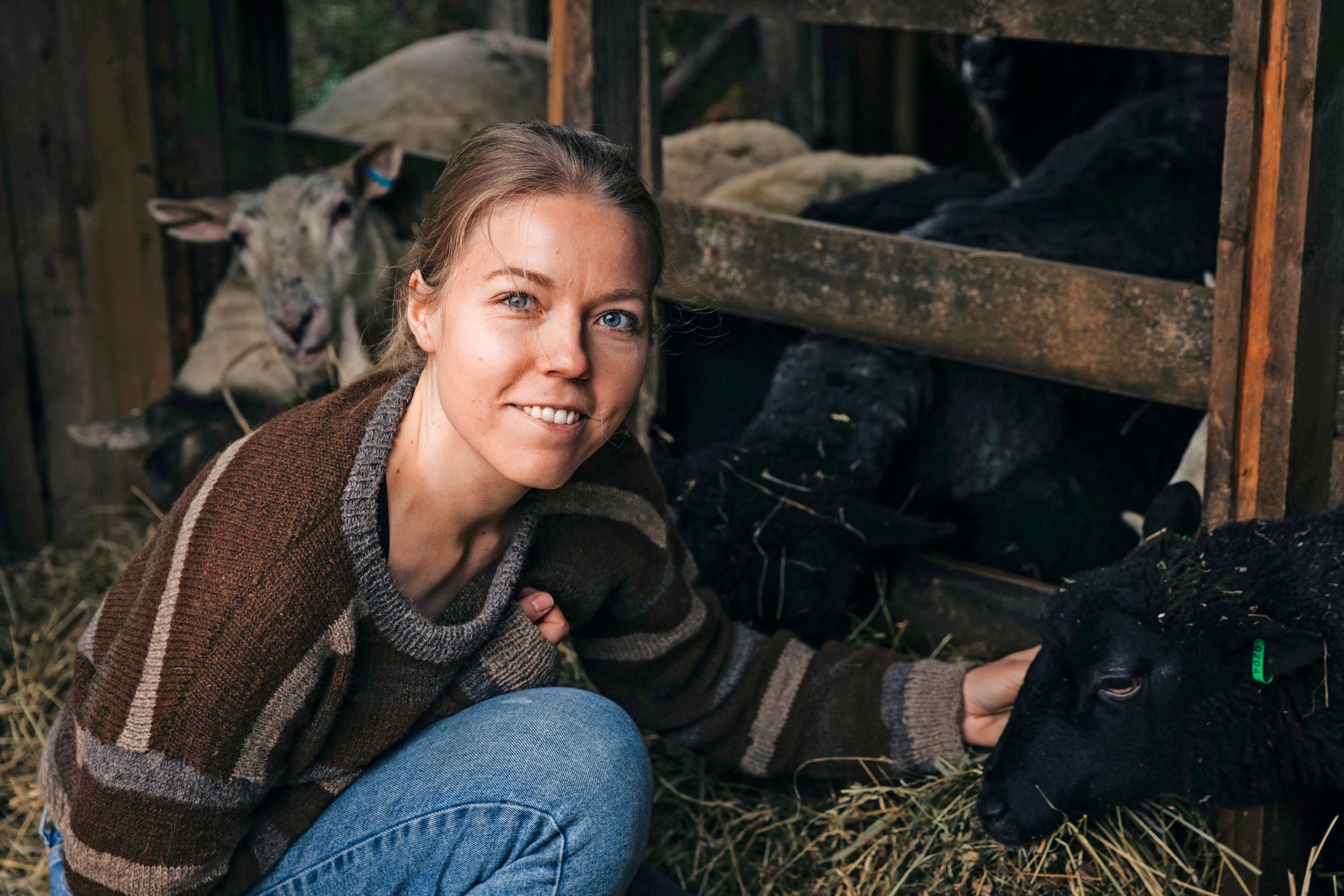 Henna Kvarnström pets a black sheep and smiles