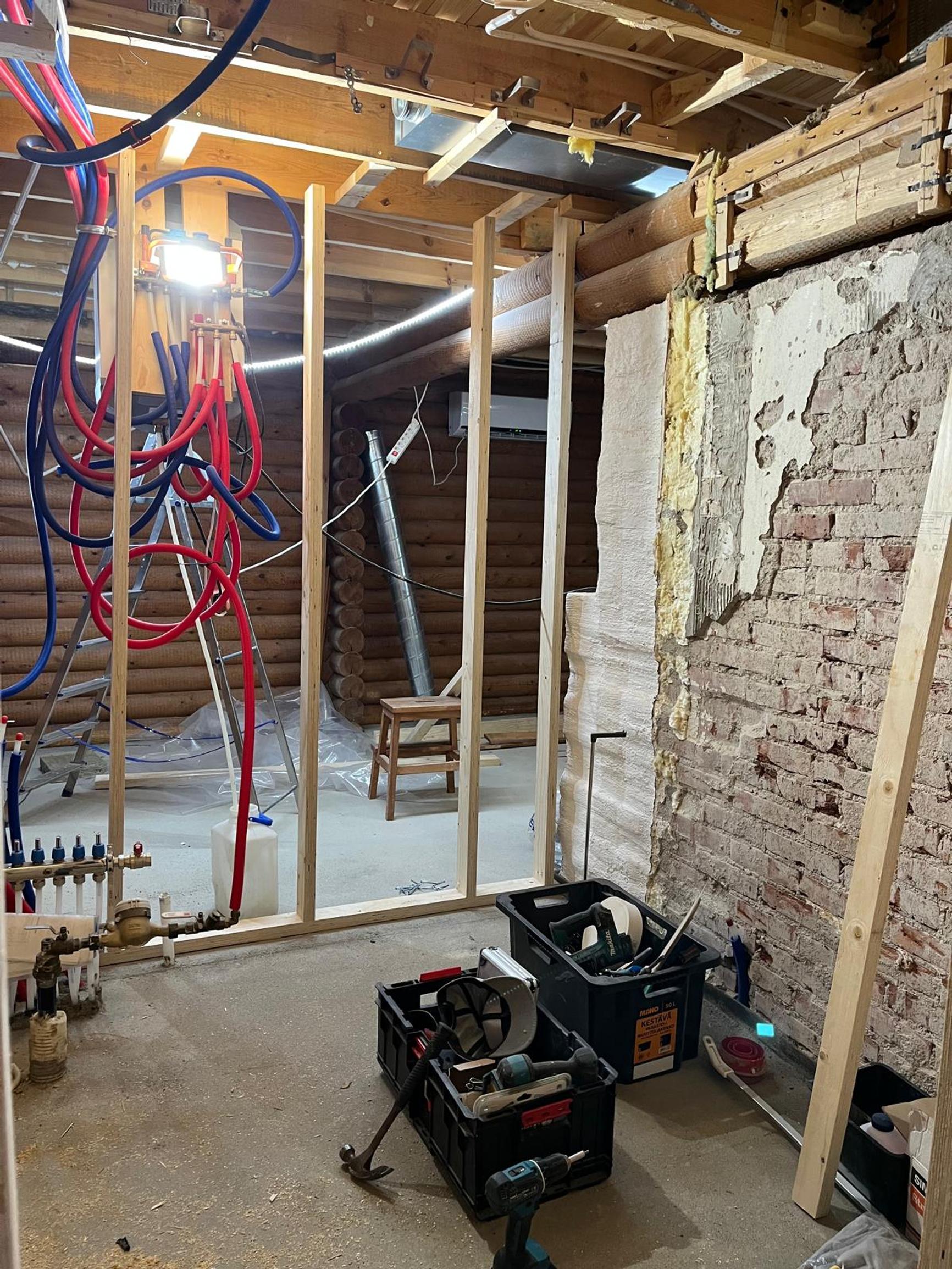 The log house has new interior wall frames and an exposed brick wall.
