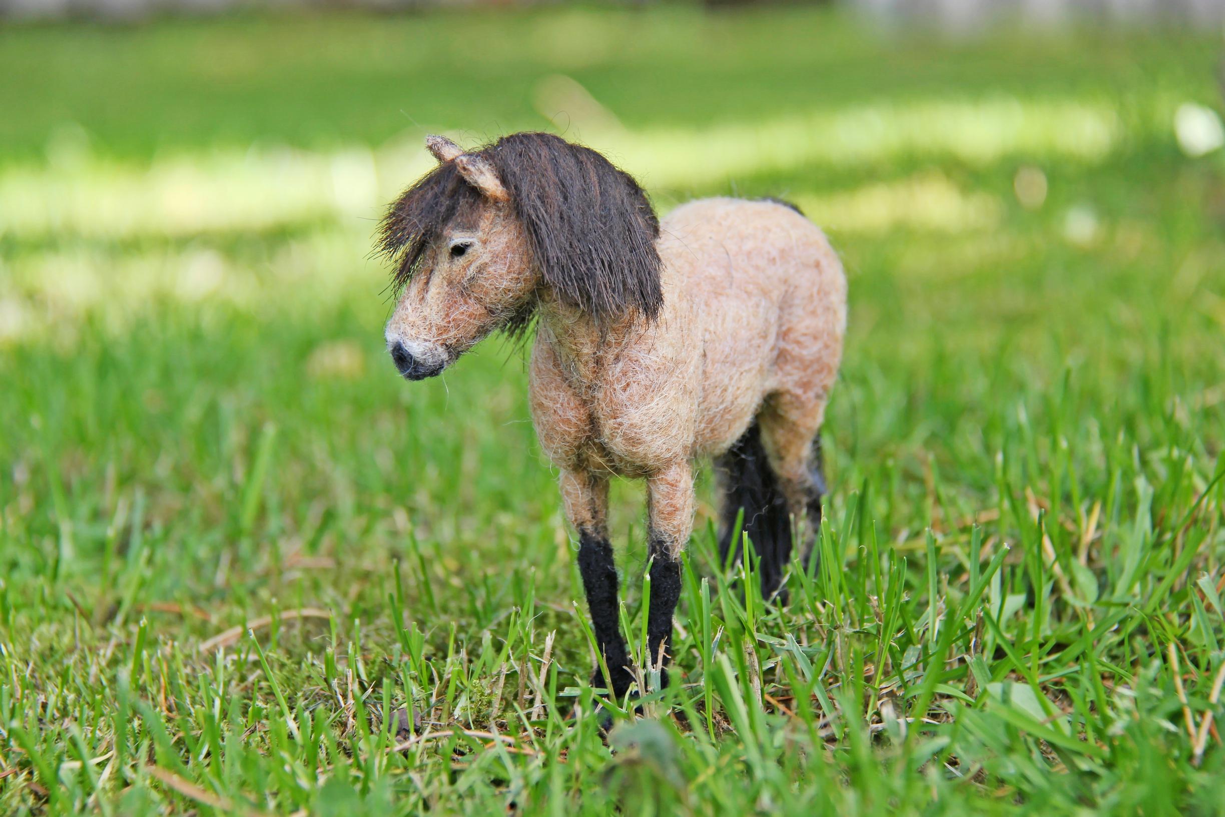 A miniature felted horse on the grass
