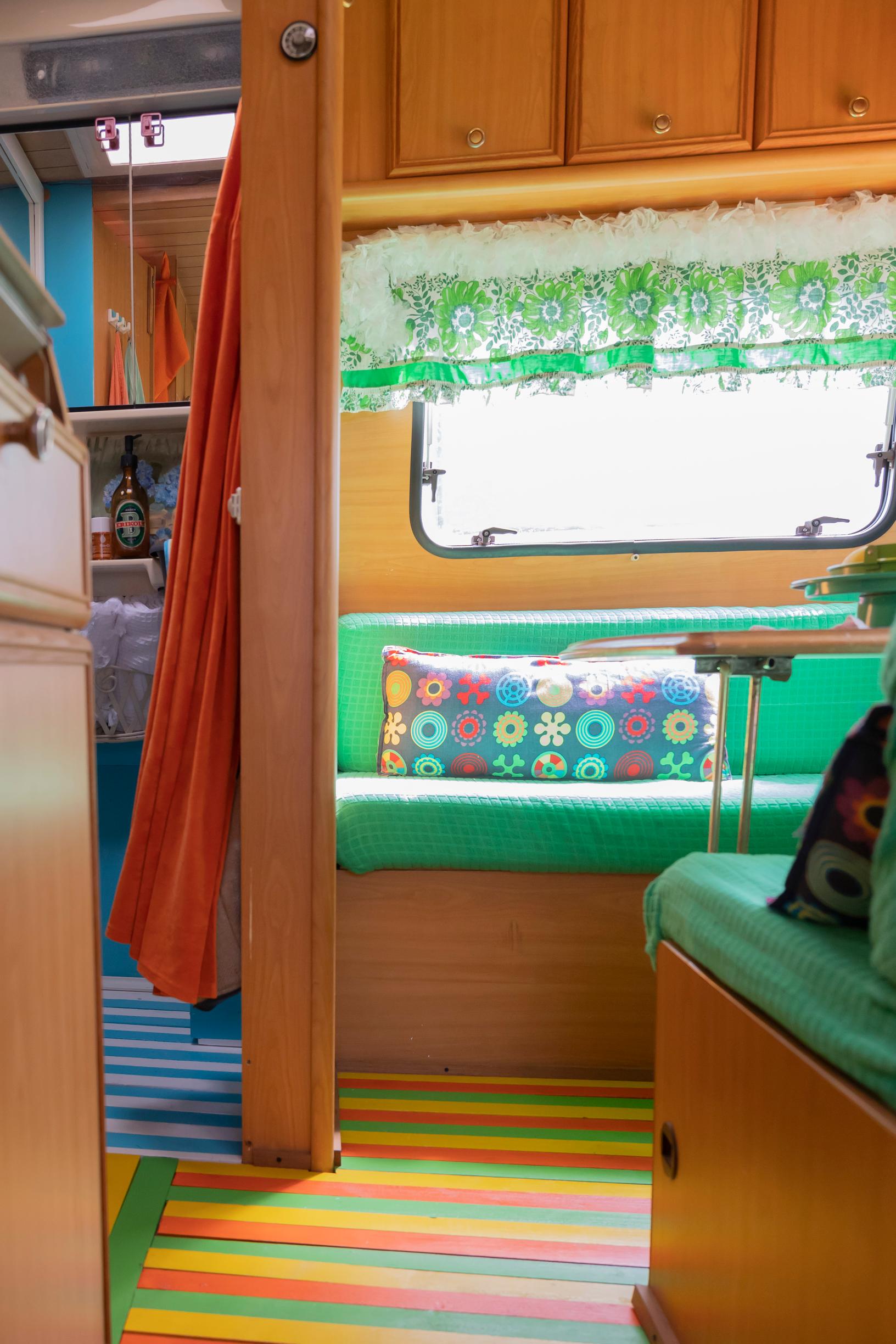 a green sofa, a colorful throw pillow and rug, and retro curtains in the travel trailer