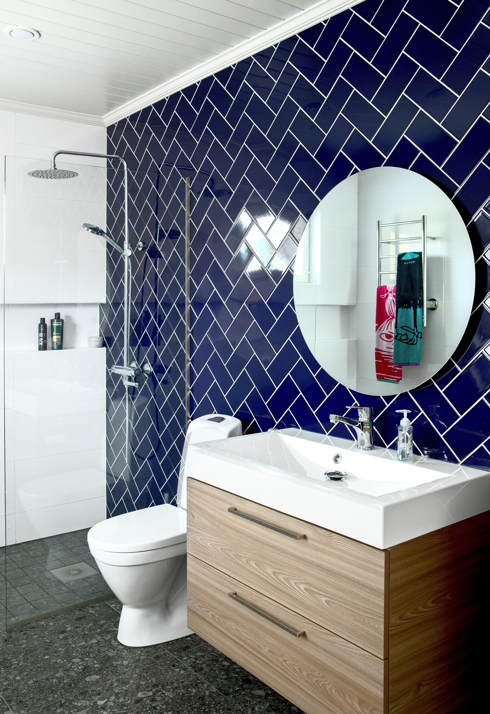 Dark blue tiled wall, gray terrazzo floor tiles, and wood-toned bathroom furniture.