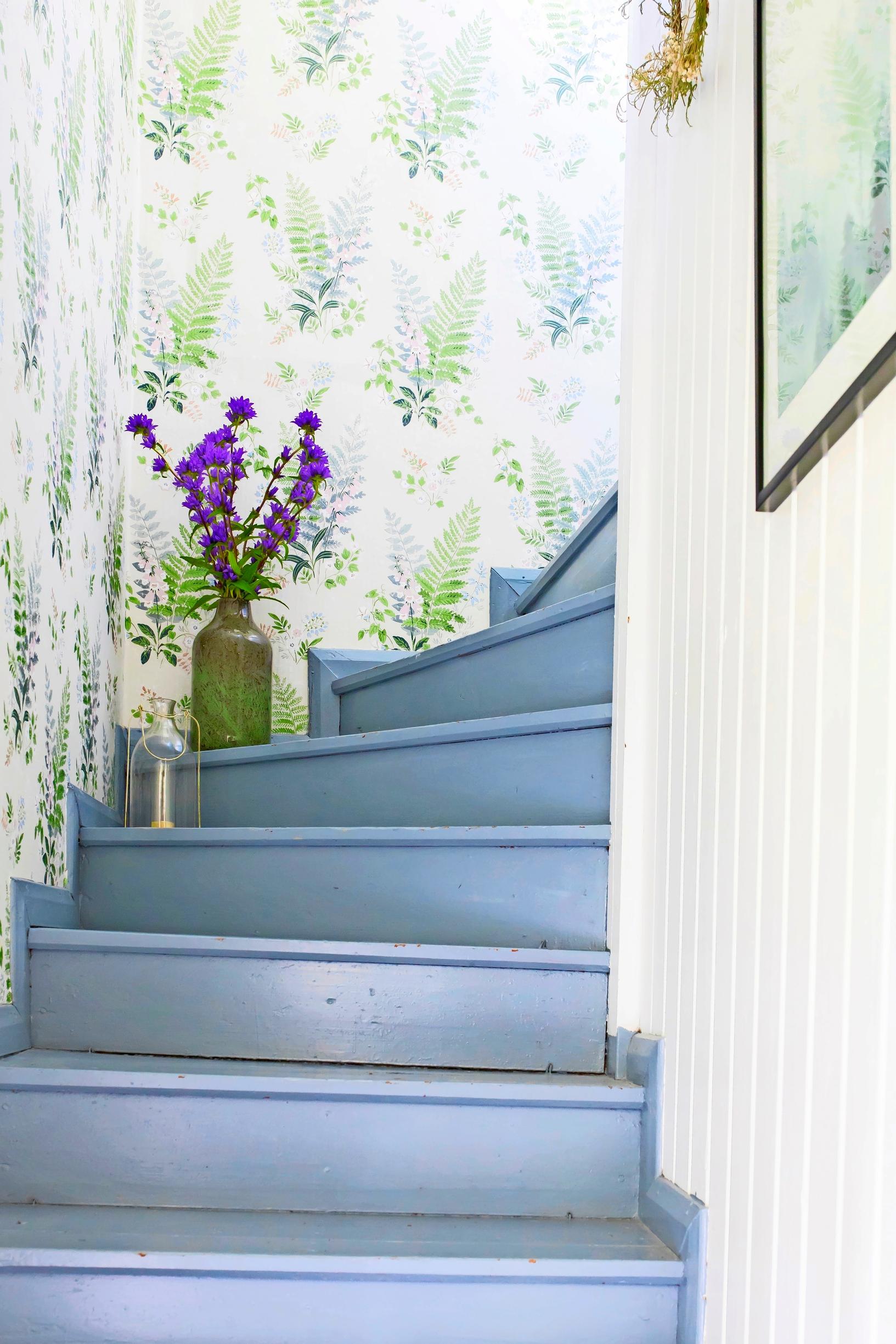 Boråstapeter’s delicate and calm Foxglove wallpaper pairs with the blue staircase of the log house