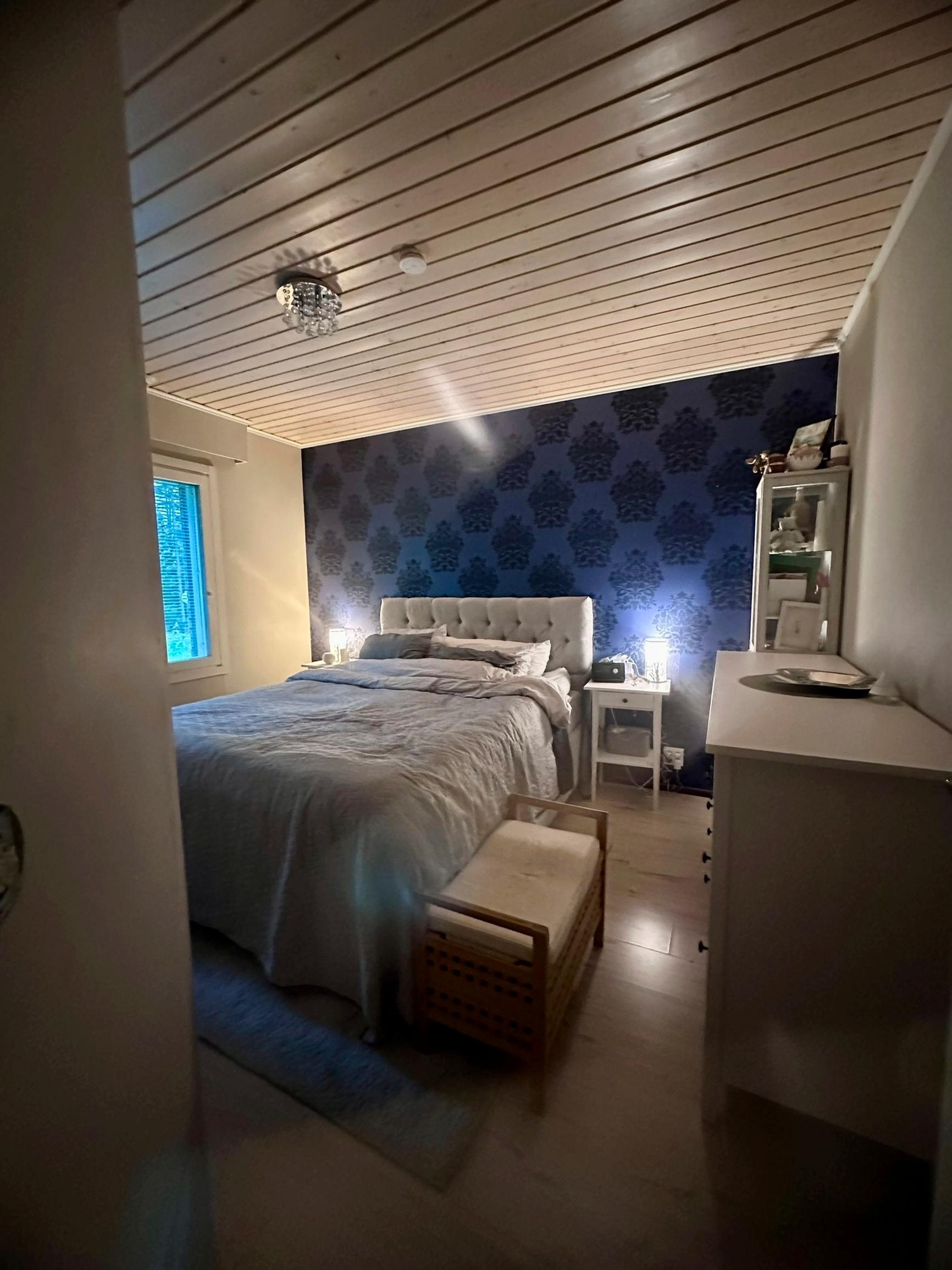 A dark, patterned wallpaper covers the bedroom’s headboard wall before the renovation.