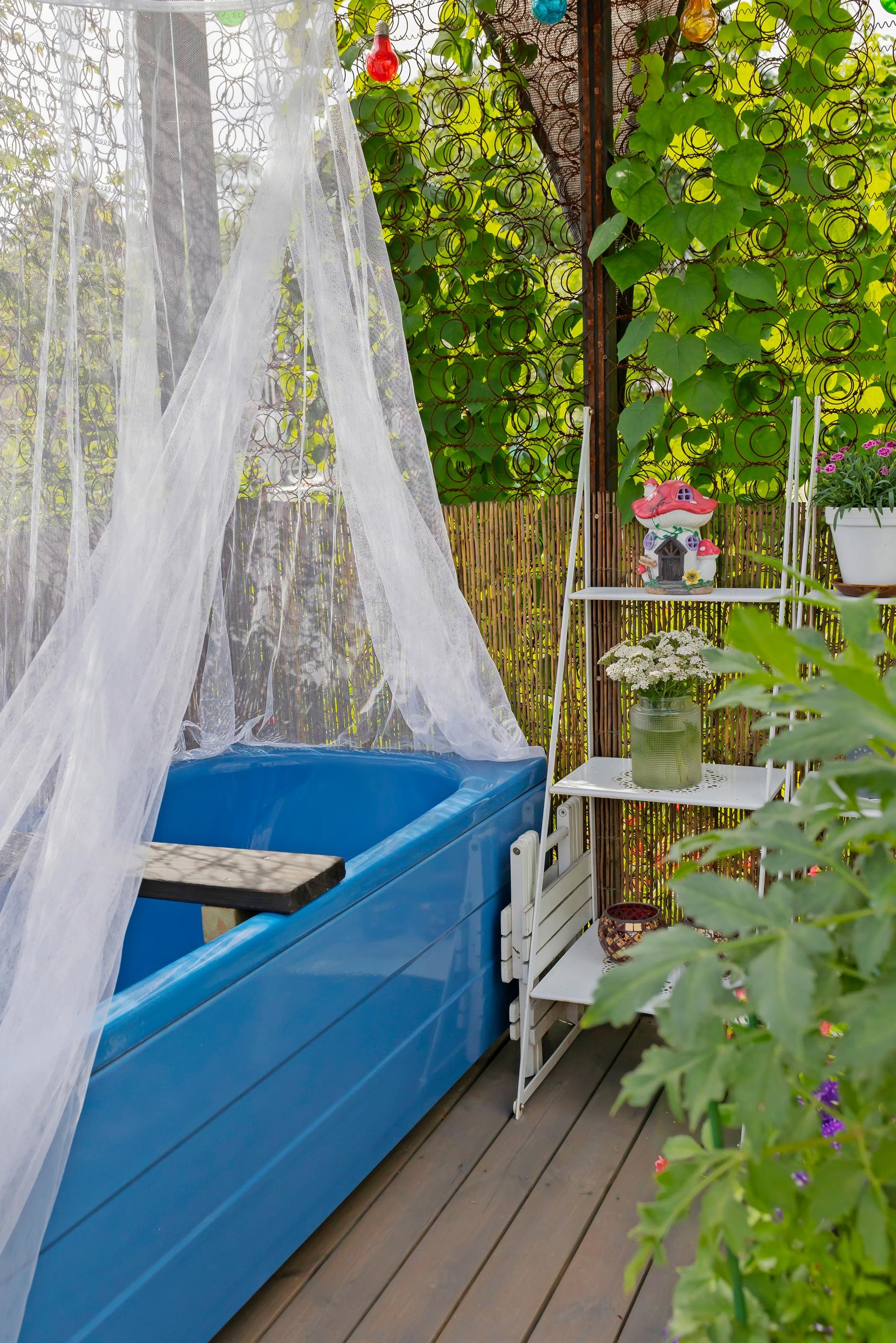 a blue tub outside on a wooden deck, a white shelf, lace curtains, and clematis vines