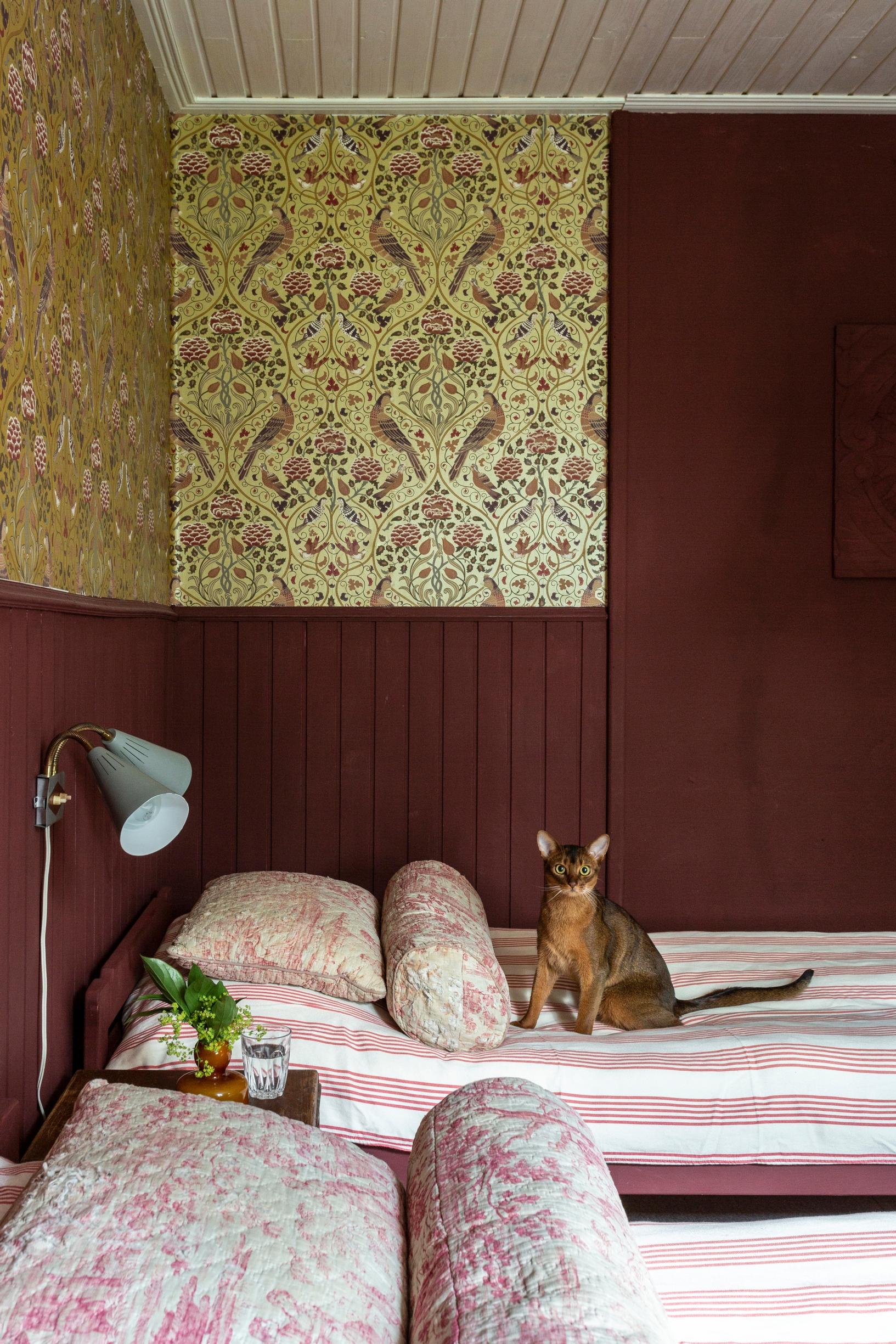 In the guest room, red half-wall paneling and William Morris’s Seasons by May Saffron wallpaper.