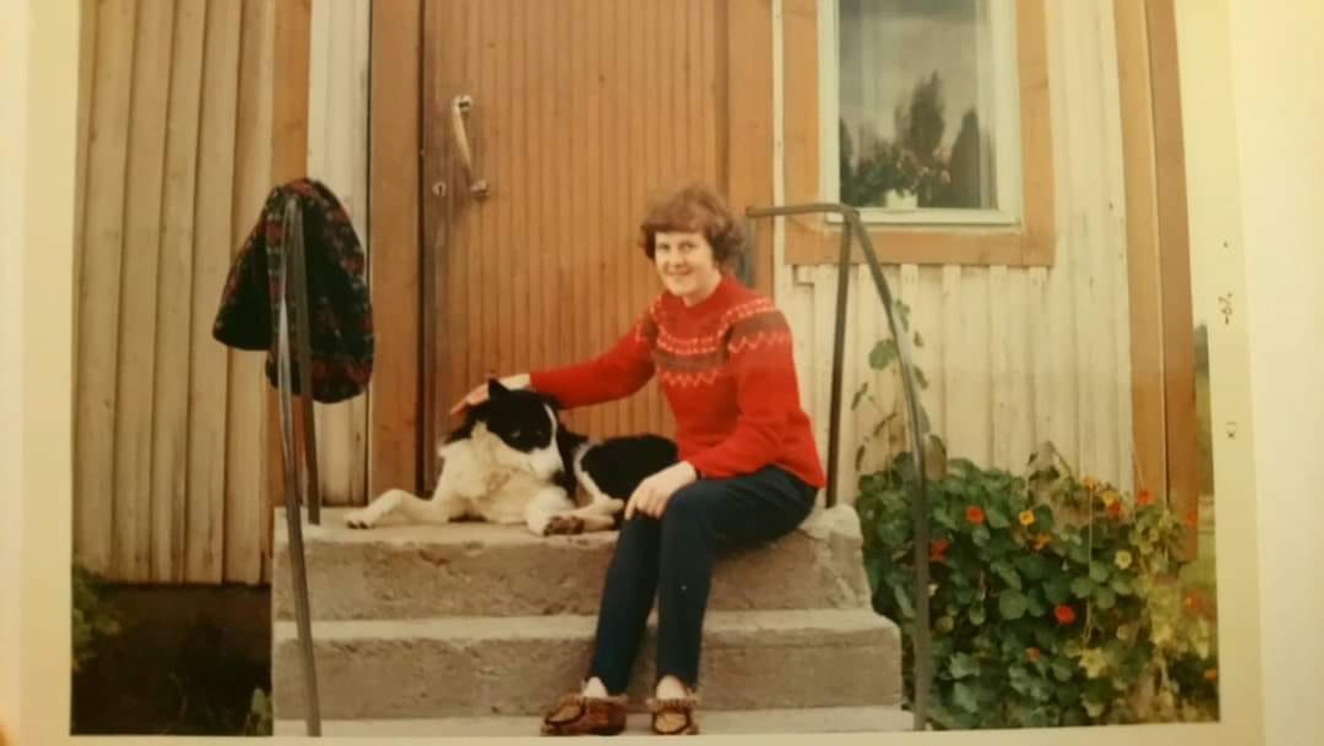 A young woman in a sweater sits on house steps with a dog beside her
