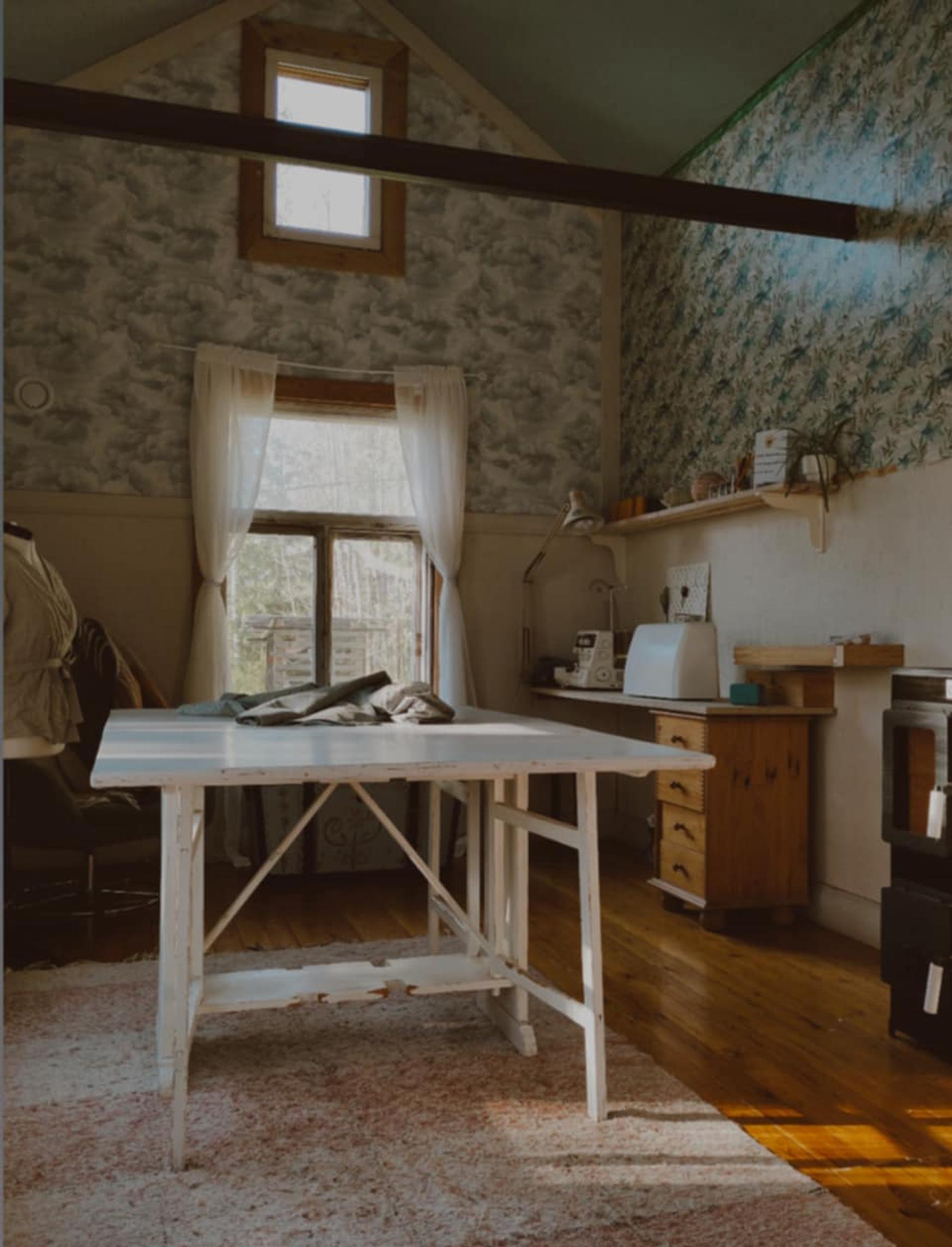 In the gabled space there’s a light wooden table, a window in the back wall, and wallpapered walls.
