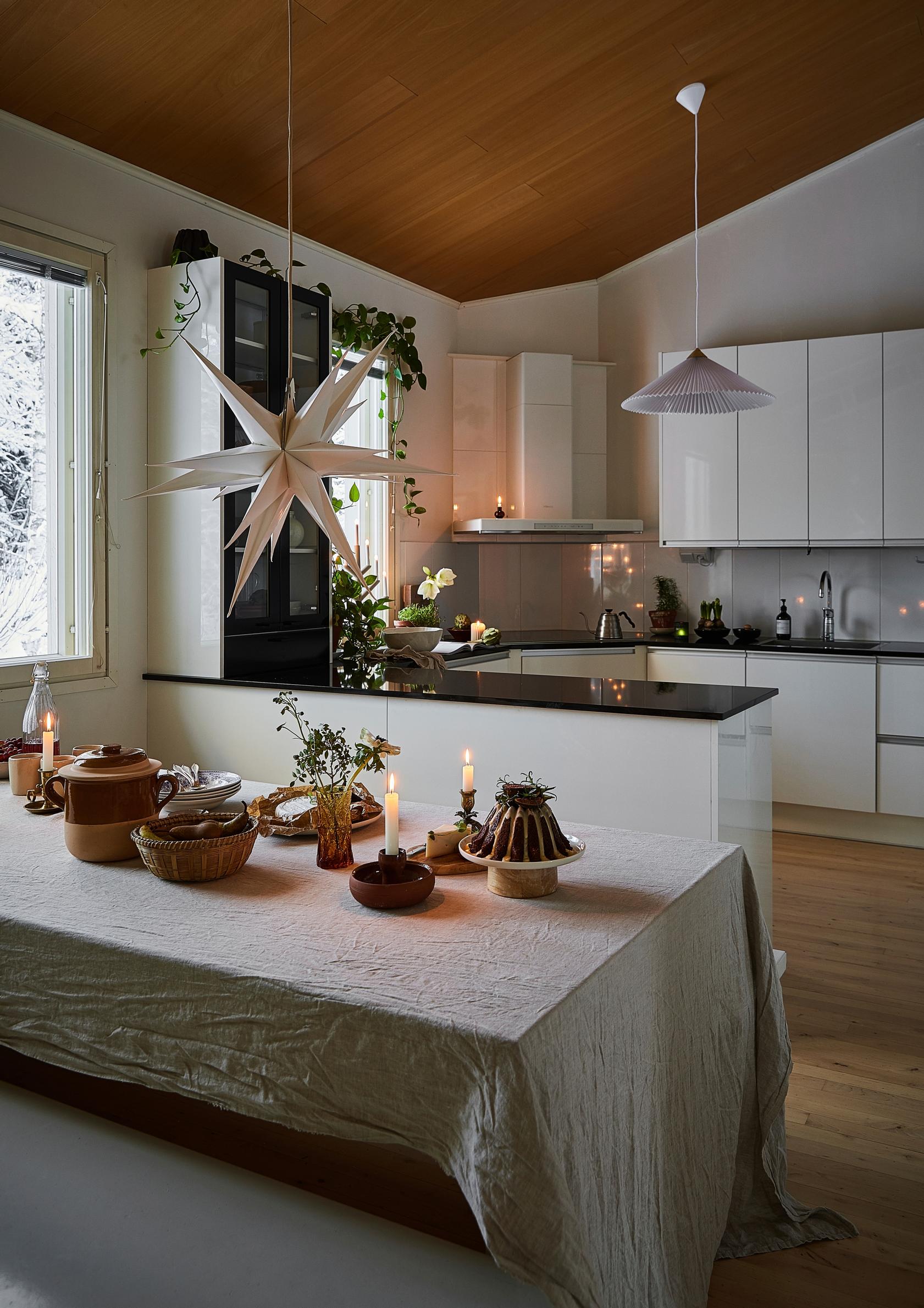 A kitchen with white cabinets and an island, a white Christmas star, a wooden ceiling, and a table set for Christmas