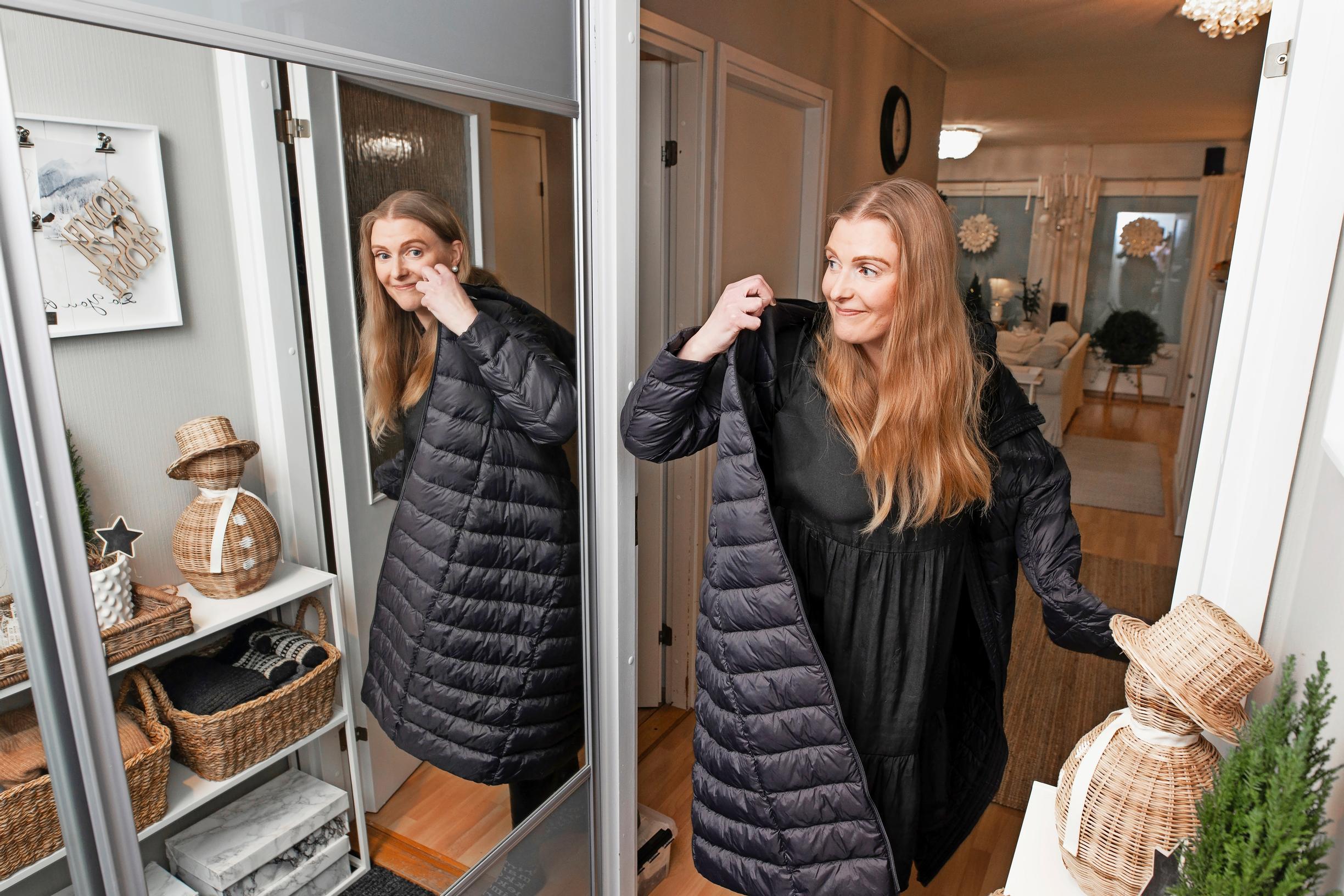 A woman looks over her shoulder in the mirror as she puts on a black puffer jacket