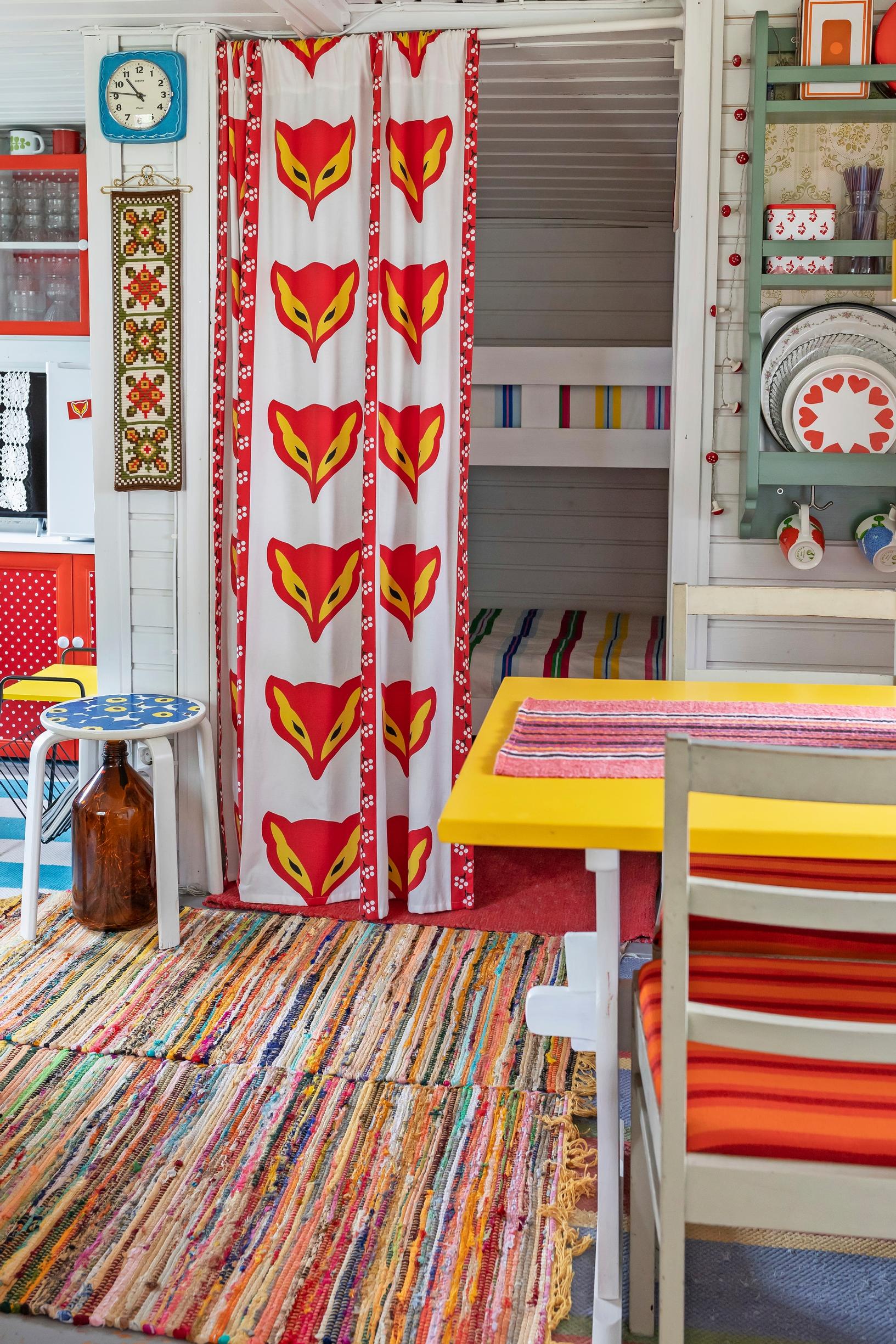 a Kettukarkki-patterned curtain, a bunk bed, rag rugs, and a dining set