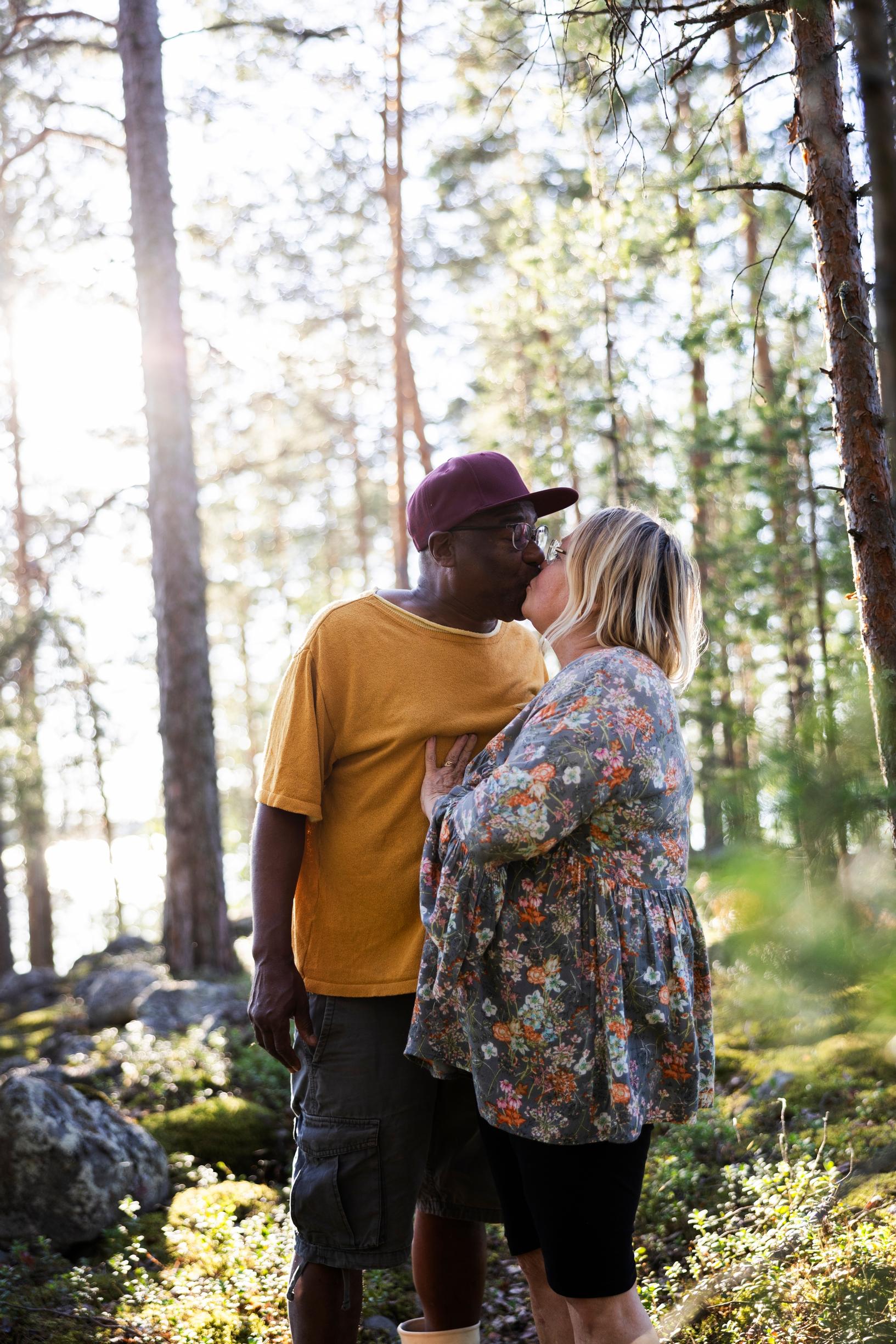 Man wearing a cap and woman in a floral shirt kissing in a summer forest
