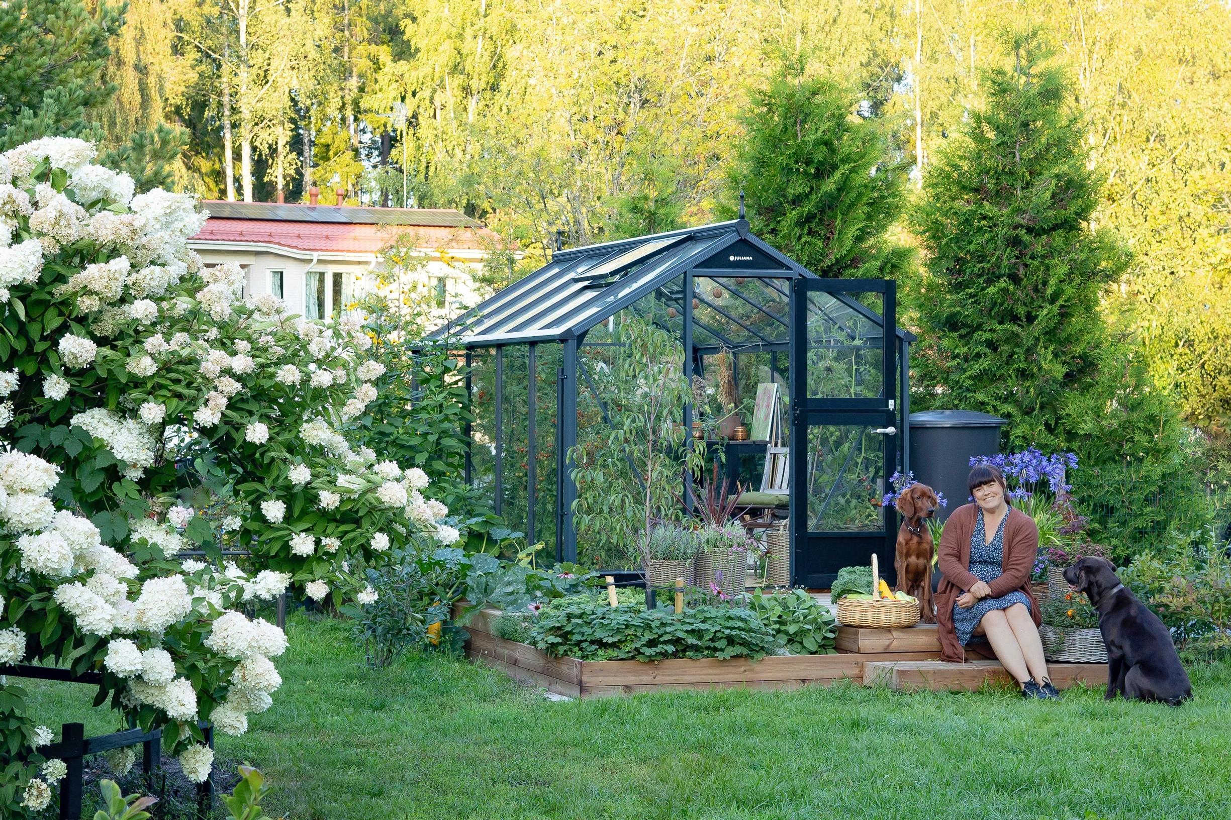 A greenhouse with Jenni Roth sitting in front with her dogs.