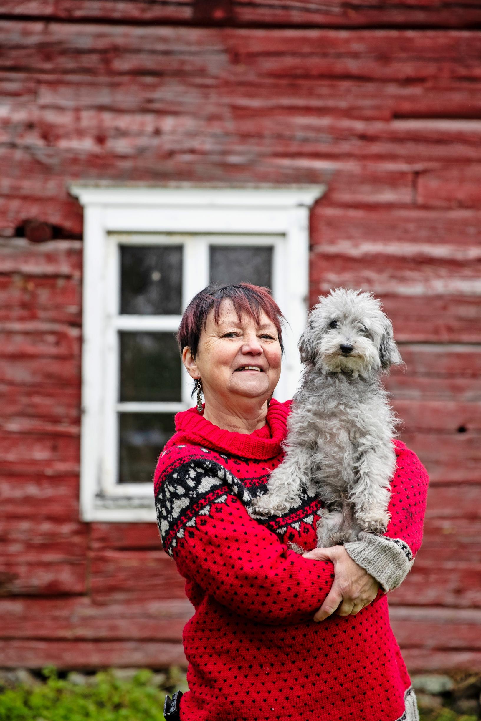 Päivi in the garden of the house, holding her dog Oliver.