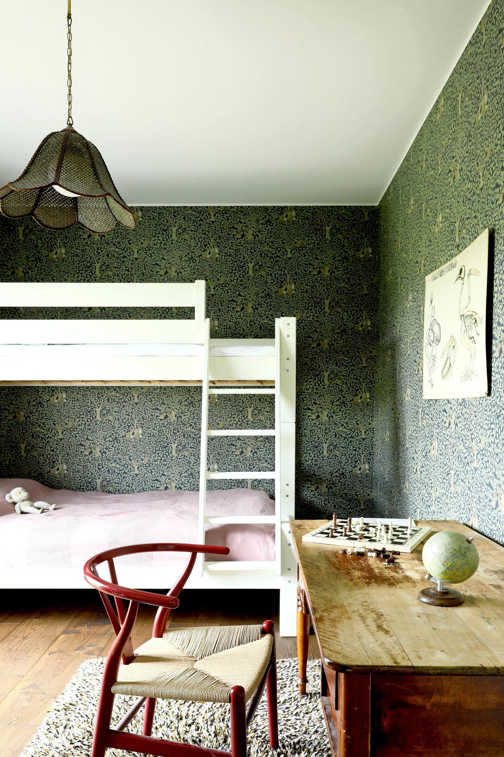 Children’s room with an old writing desk and a chair with rattan seat. A white bunk bed in the background.