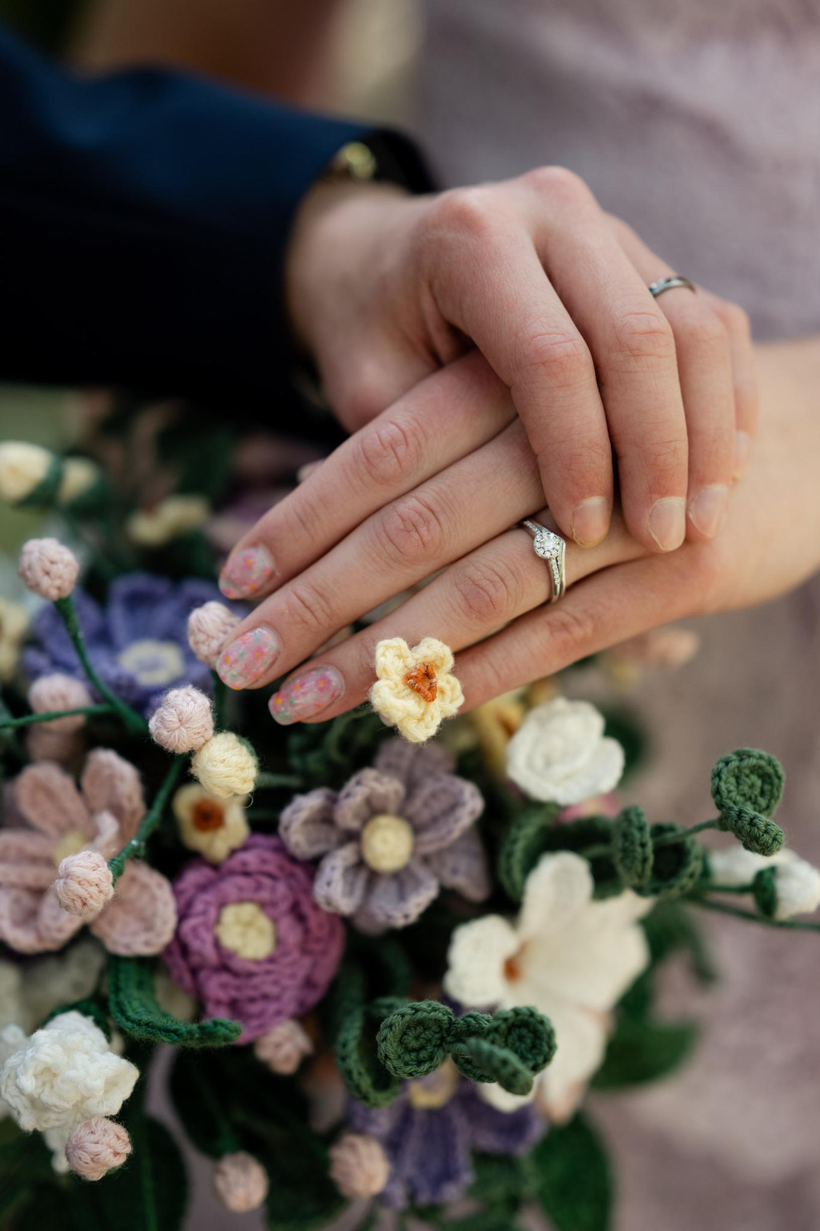 A close-up of the bride’s hand wearing her engagement ring, with the crocheted bouquet in the background.