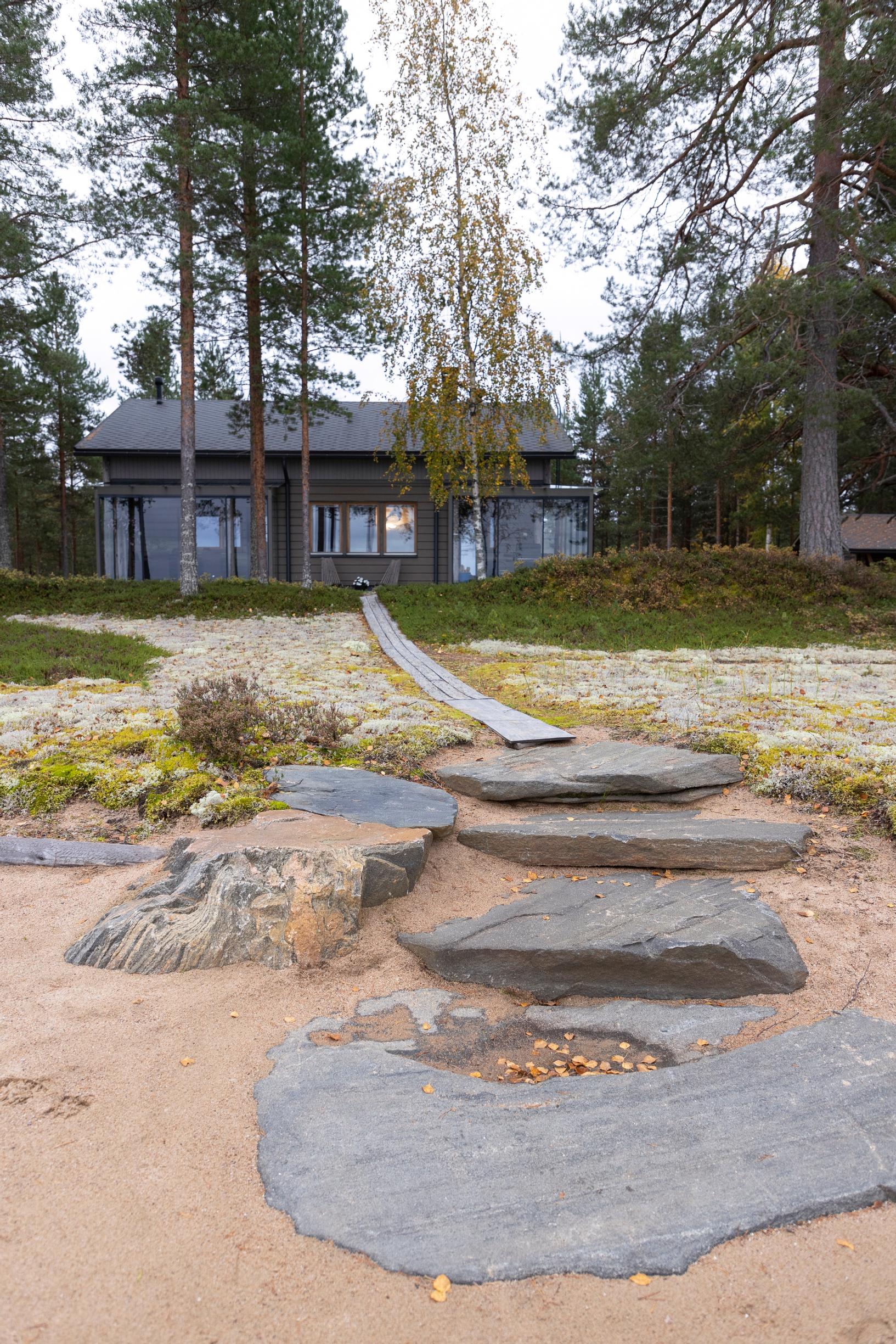 Large rocks on the beach, with a boardwalk leading to the cabin, forest in the background