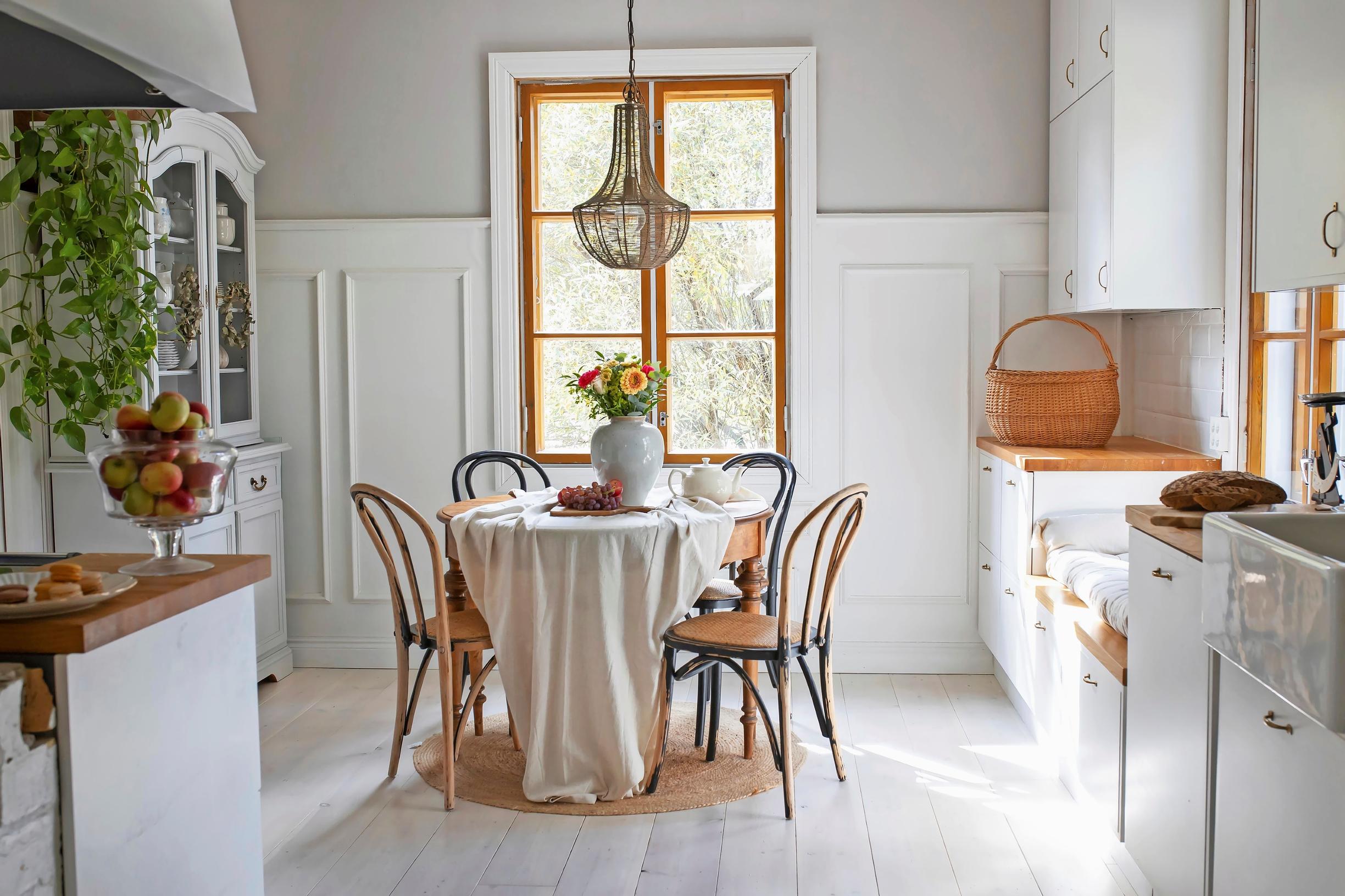 The kitchen’s end wall features white paneling. The upper part of the wall is light gray. In the center of the room is a round dining set.