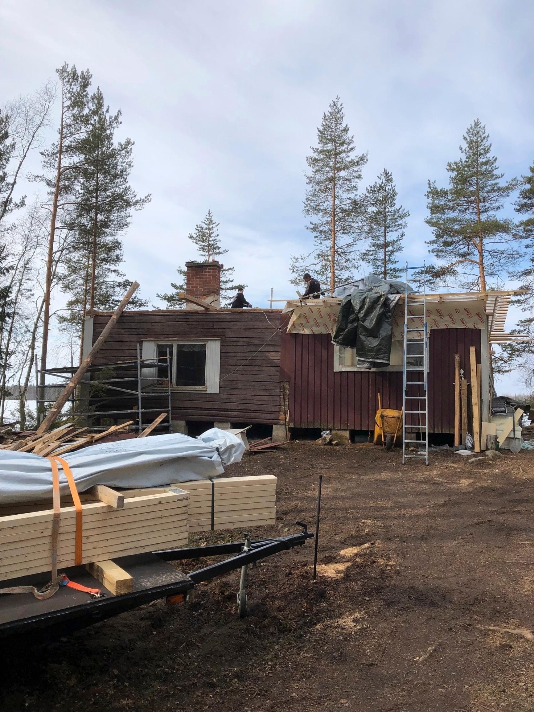 A torn-down log cottage under renovation with new boards; forest in the background