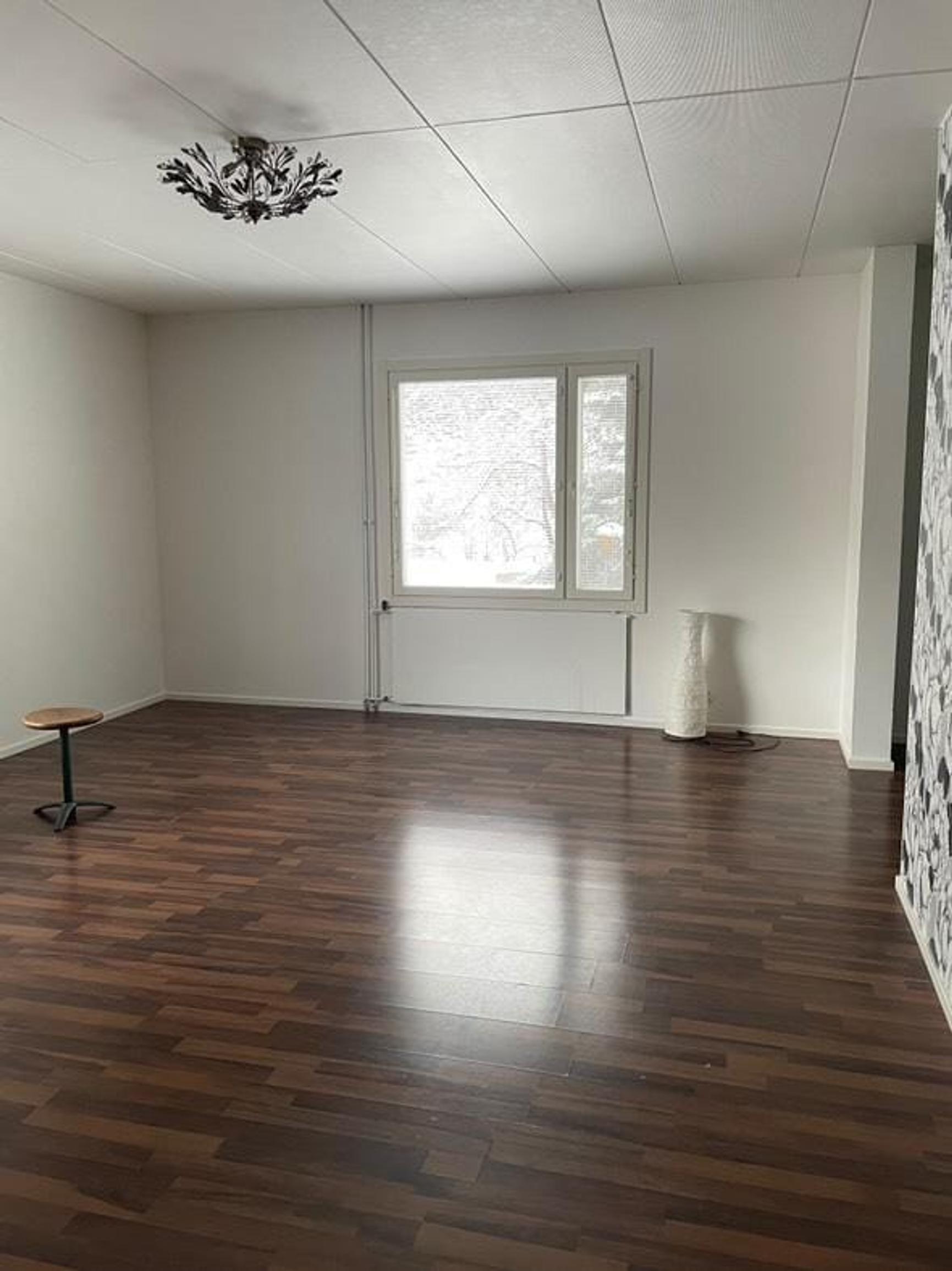 In an empty room with a dark floor, a black-and-white wallpapered wall, and a window on the back wall