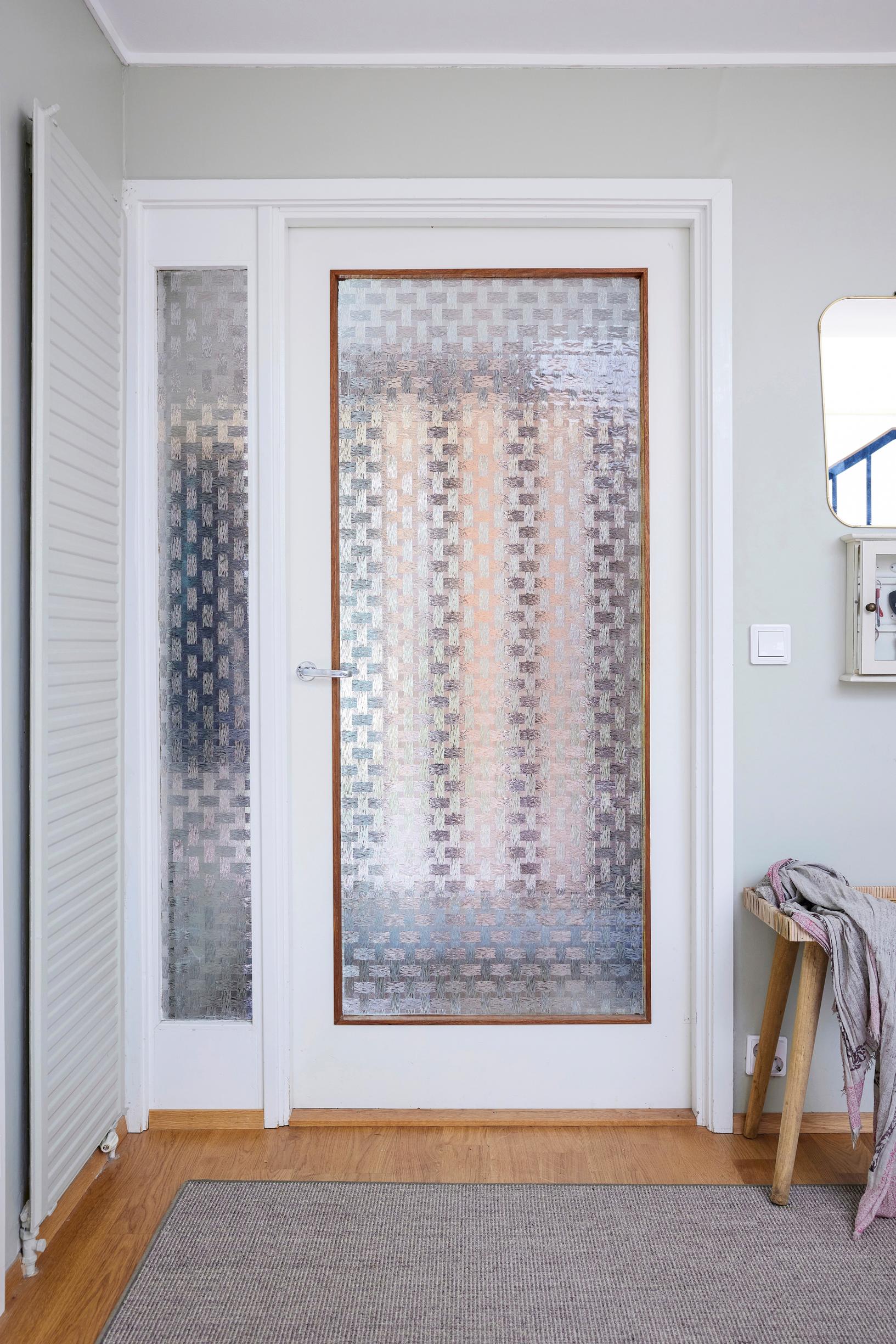 The center of the white-framed door is patterned glass. Beside the door is a narrow, door-height side window with the same patterned glass.