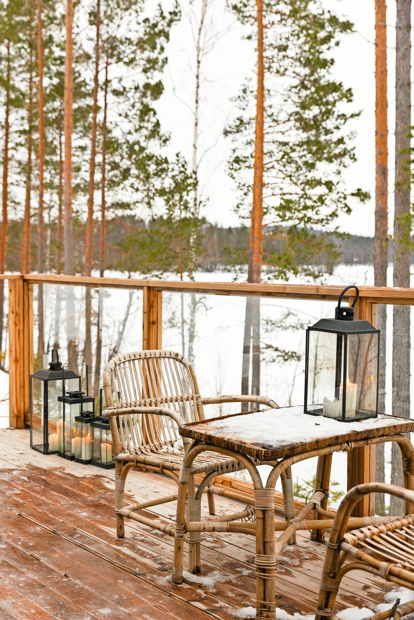 A rattan table set on the terrace with lanterns, overlooking a snowy lake.