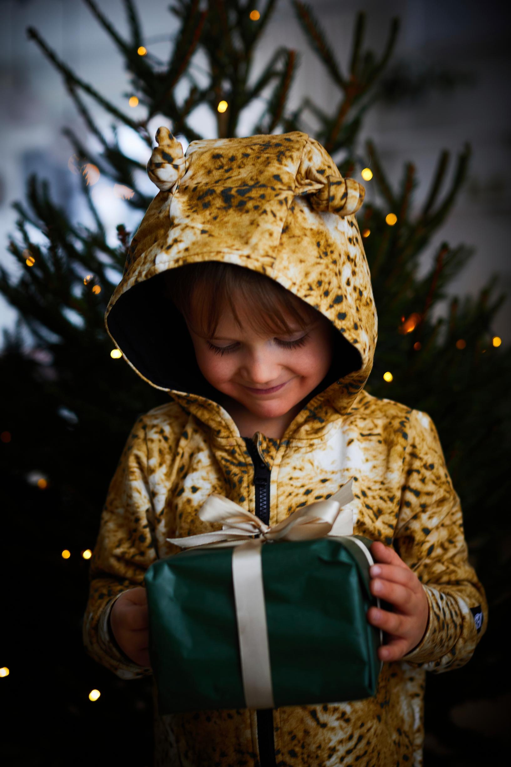 a boy holding a gift with a Christmas tree in the background