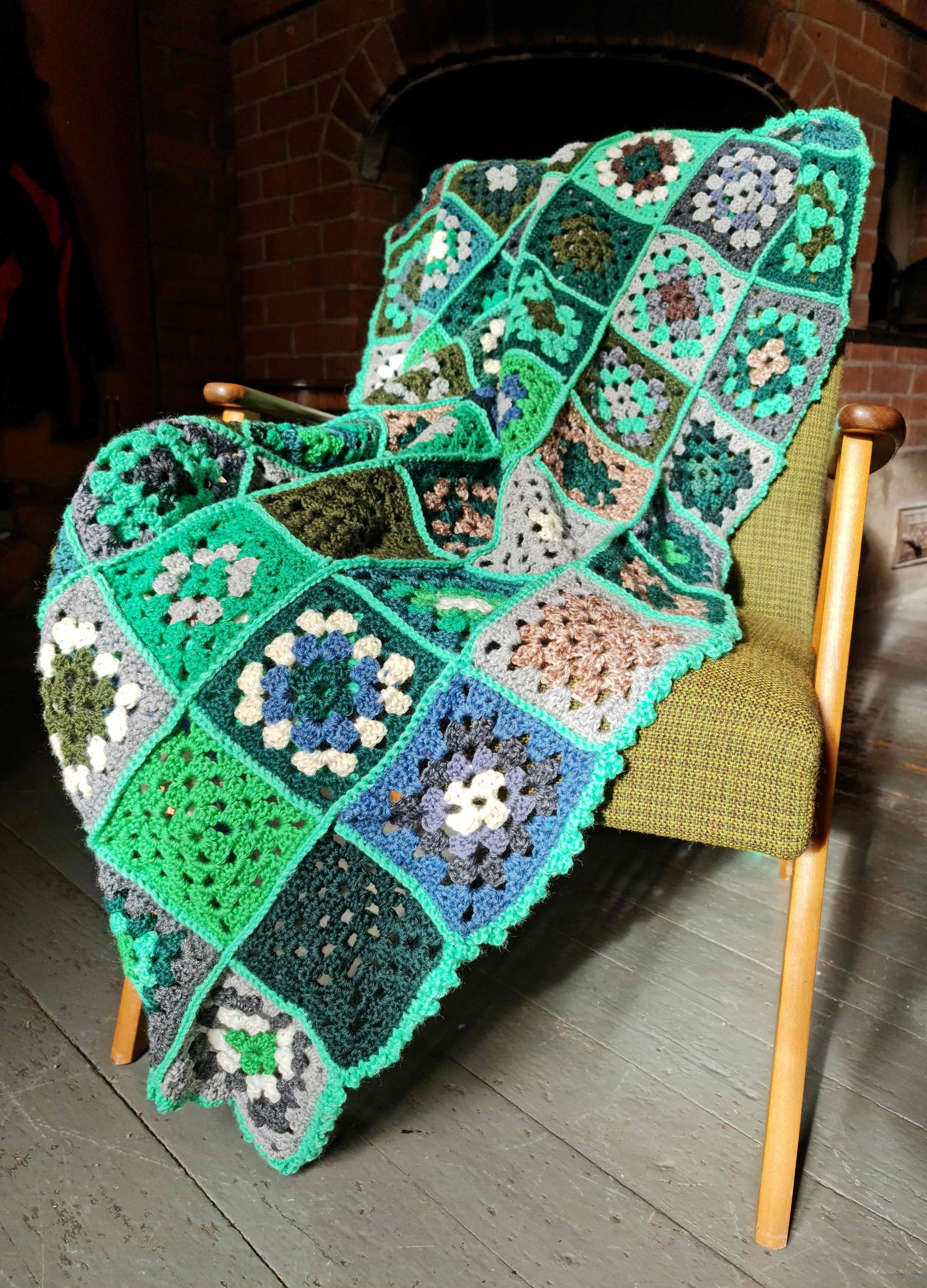 A green-toned throw blanket crocheted by Jani Kylmälä with granny squares, draped over an armchair