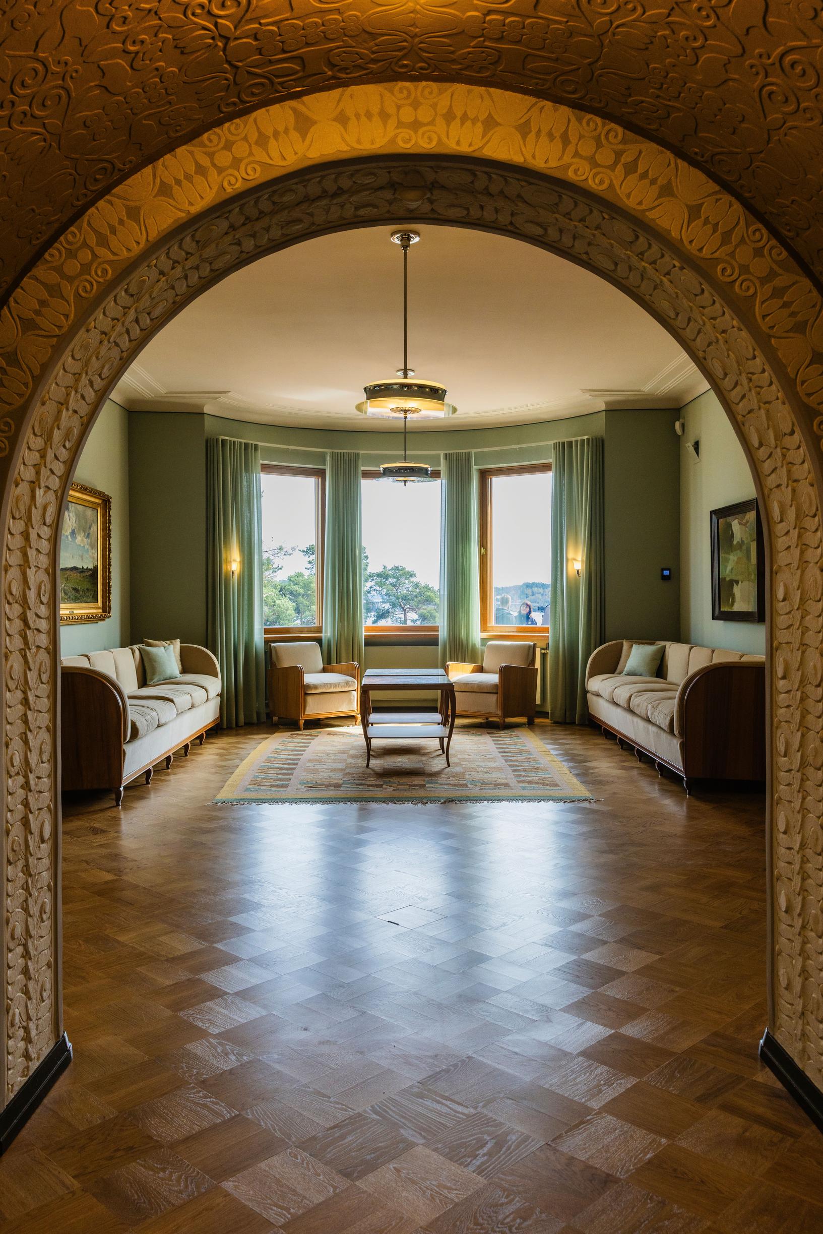 Kultaranta’s living room with a parquet floor and seating area, an arch in the foreground