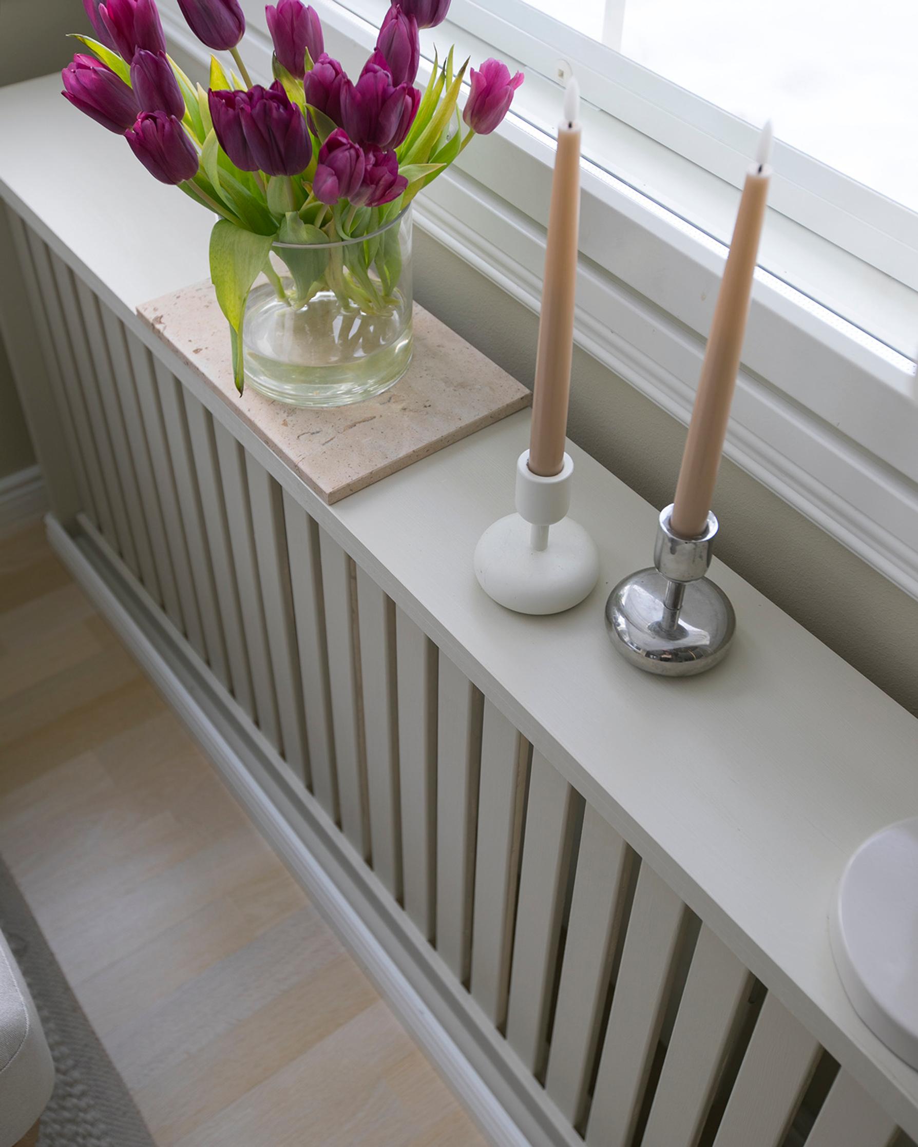 A finished radiator cover with candles and a flower vase on top